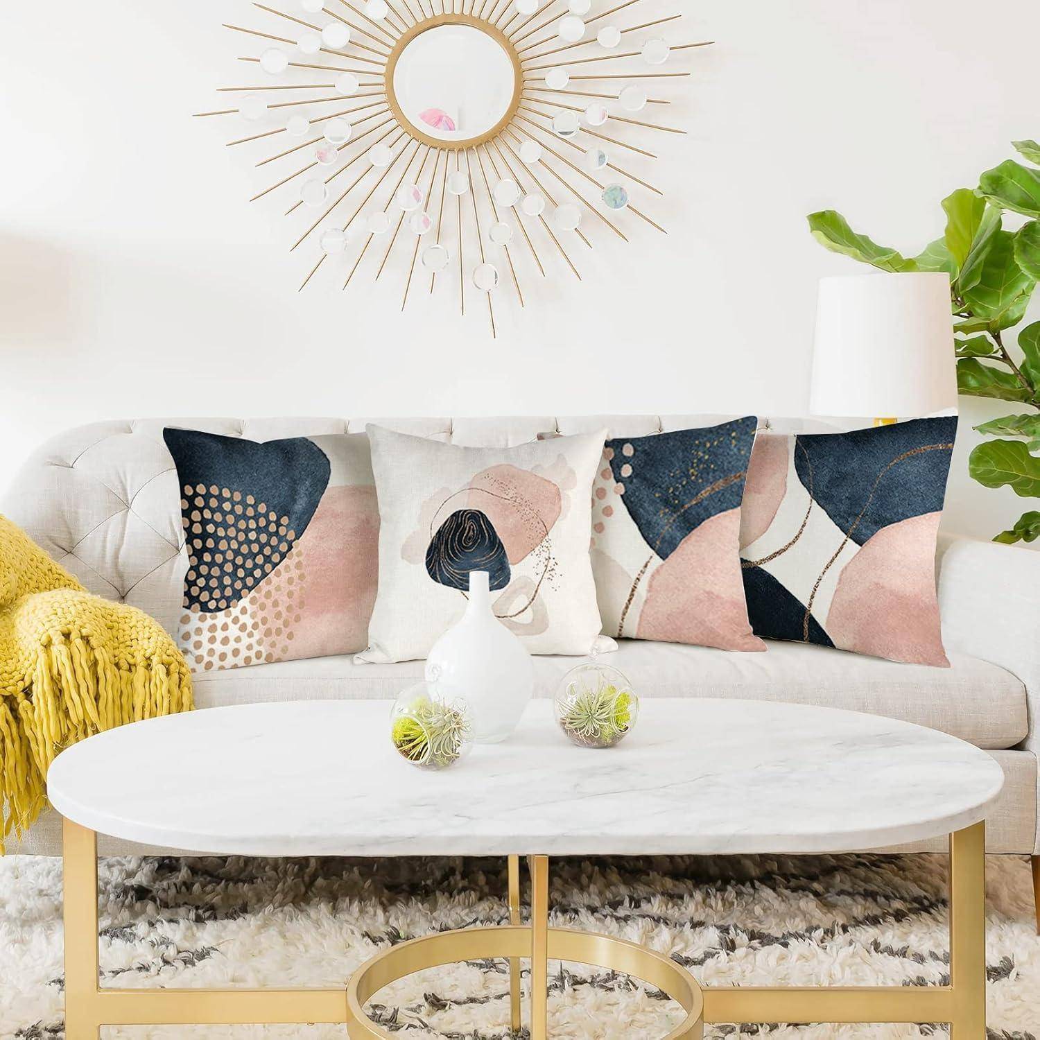 Ein Wohnzimmer mit einem weißen Sofa, geschmückt mit abstrakten gemusterten Kissen, einem runden Spiegel mit einem Sonnenstrahlen-Rahmen und einem modernen Couchtisch.