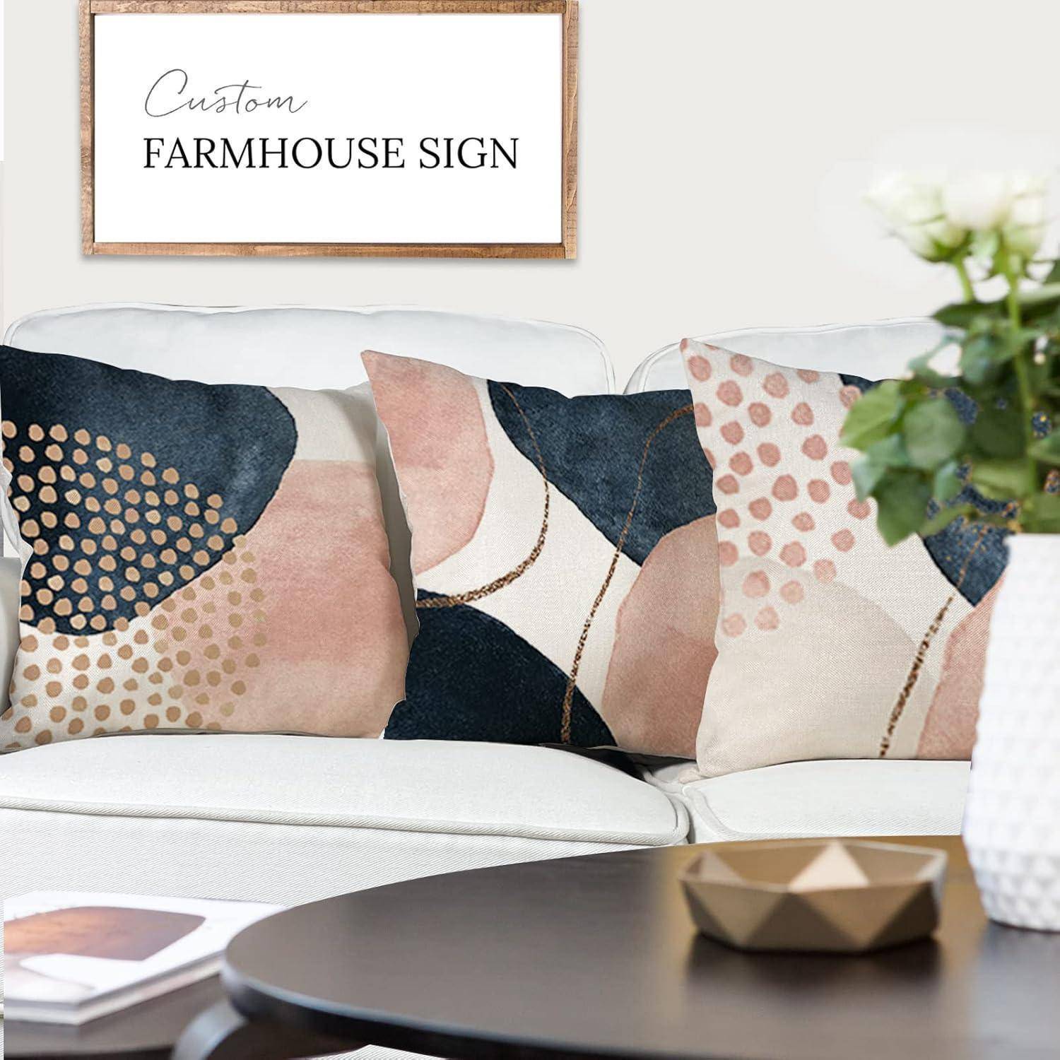 Zwei dekorative Kissen mit abstrakten Mustern liegen auf einem weißen Sofa unter einem gerahmten Schild mit der Aufschrift „Custom Farmhouse Sign