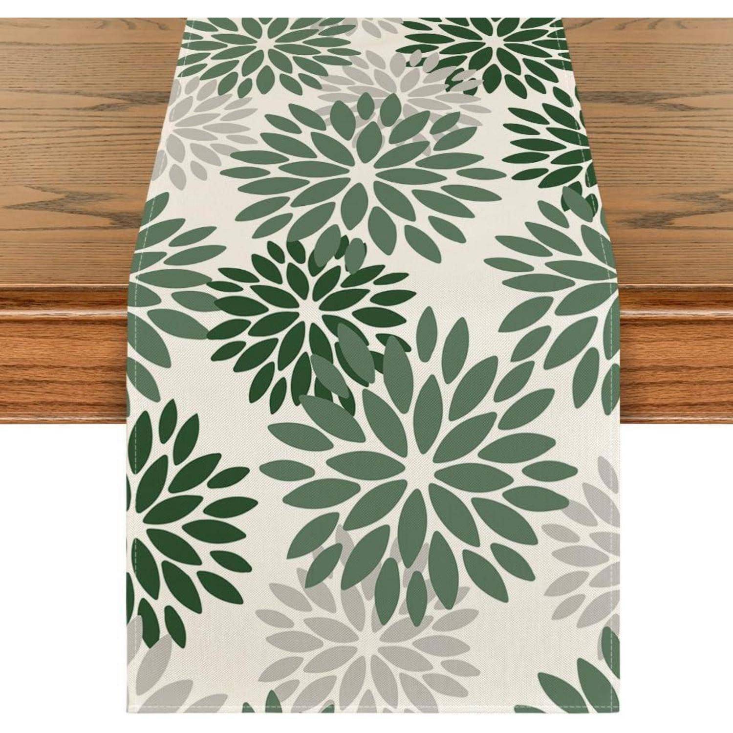 Ein Holztisch mit einem Tischläufer mit Blumenmuster, der grüne und graue Blumen auf cremefarbenem Hintergrund zeigt.