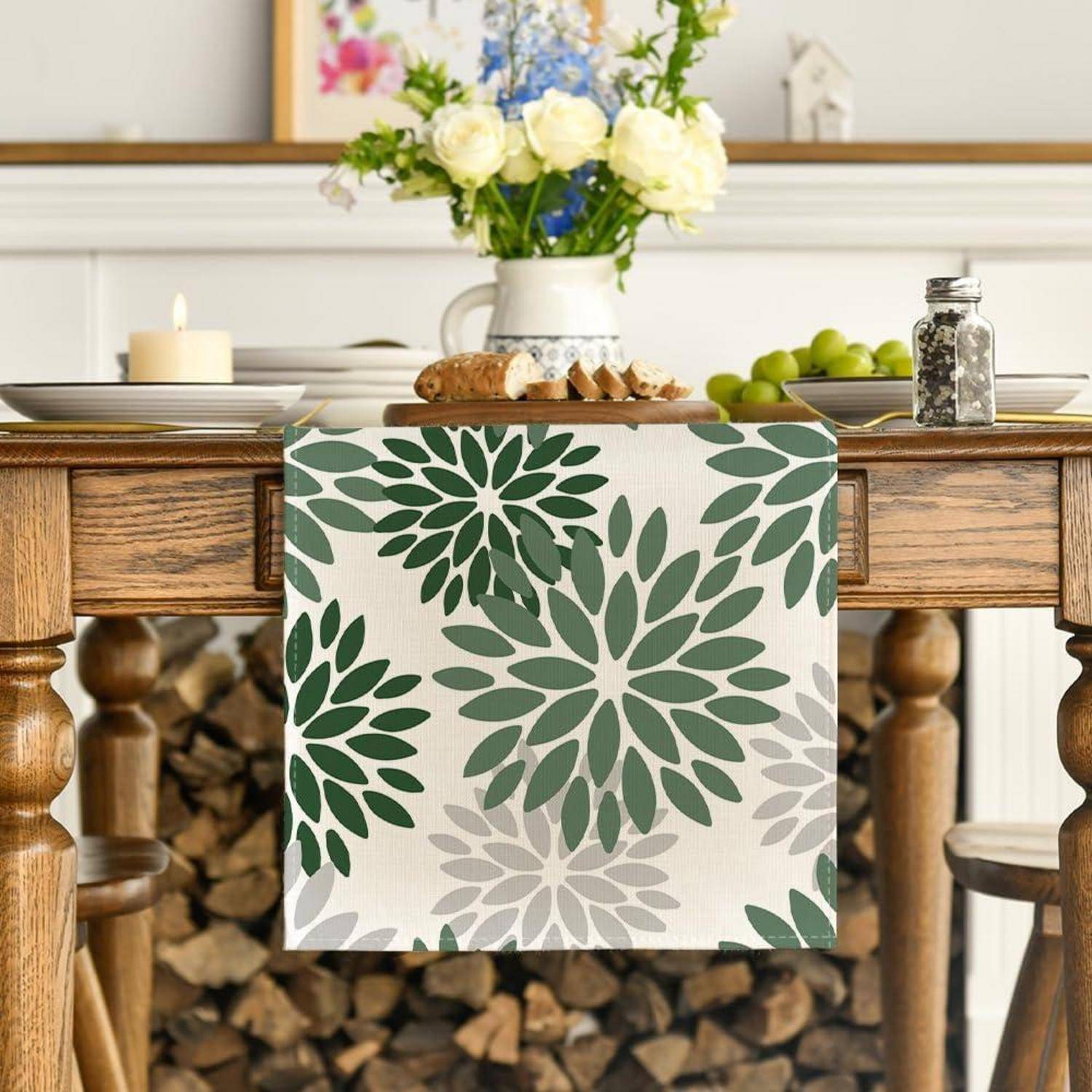 Ein Holztisch trägt ein Tuch mit Blumenmuster und eine Vase mit weißen und blauen Blumen. Kerzen und ein Gemälde schmücken den Hintergrund.