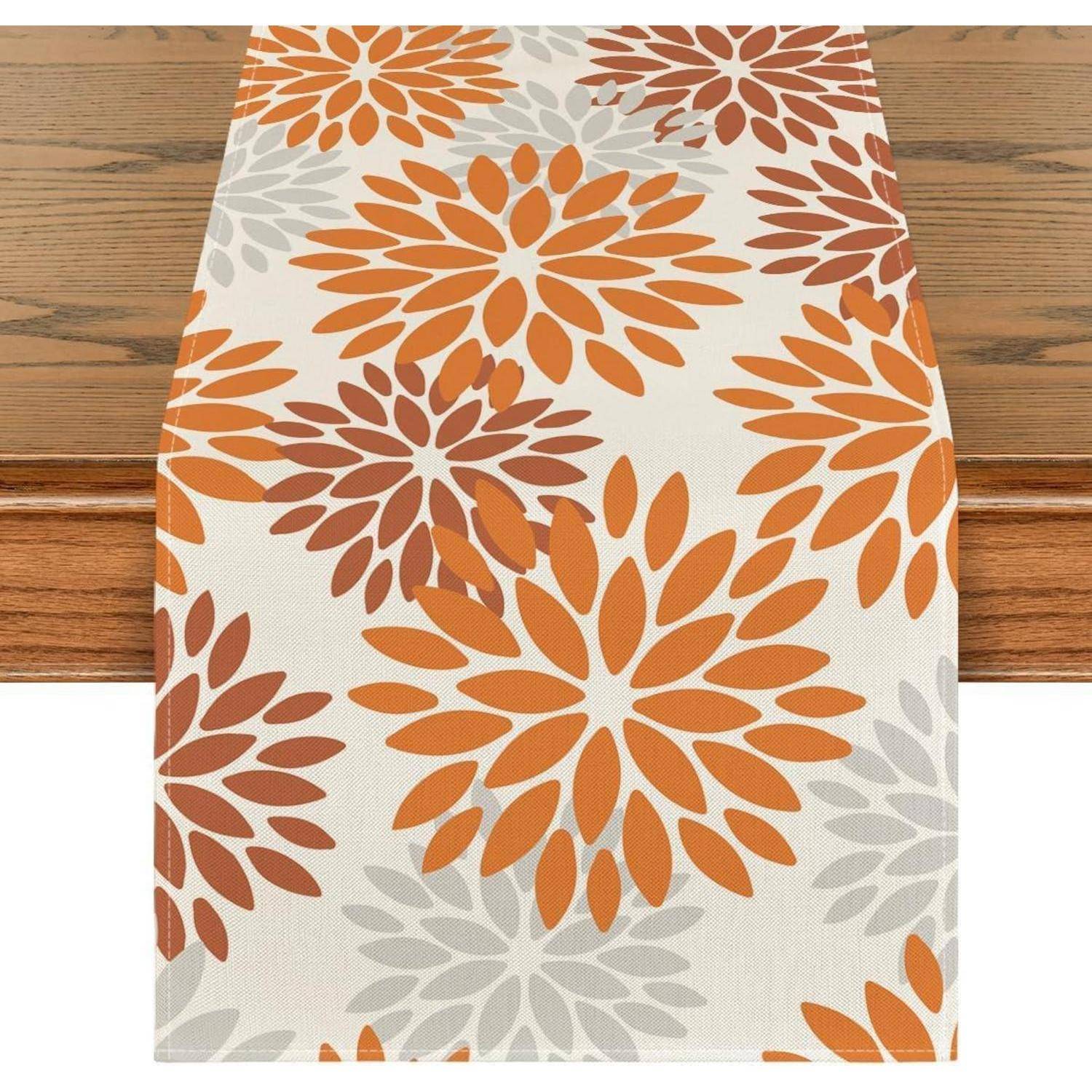 Ein Tischläufer mit einem Blumenmuster in Orange, Rot und Grau auf einem Holztisch. Das Design zeigt überlappende Blumenformen.