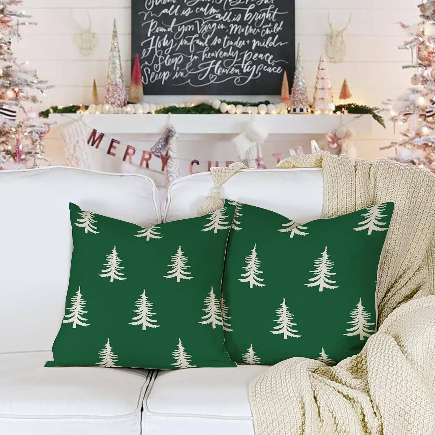 Festlicher Wohnraum mit Weihnachtsdekoration; zwei grüne Kissen mit weißen Bäumen auf einem weißen Sofa und einem Banner mit der Aufschrift 