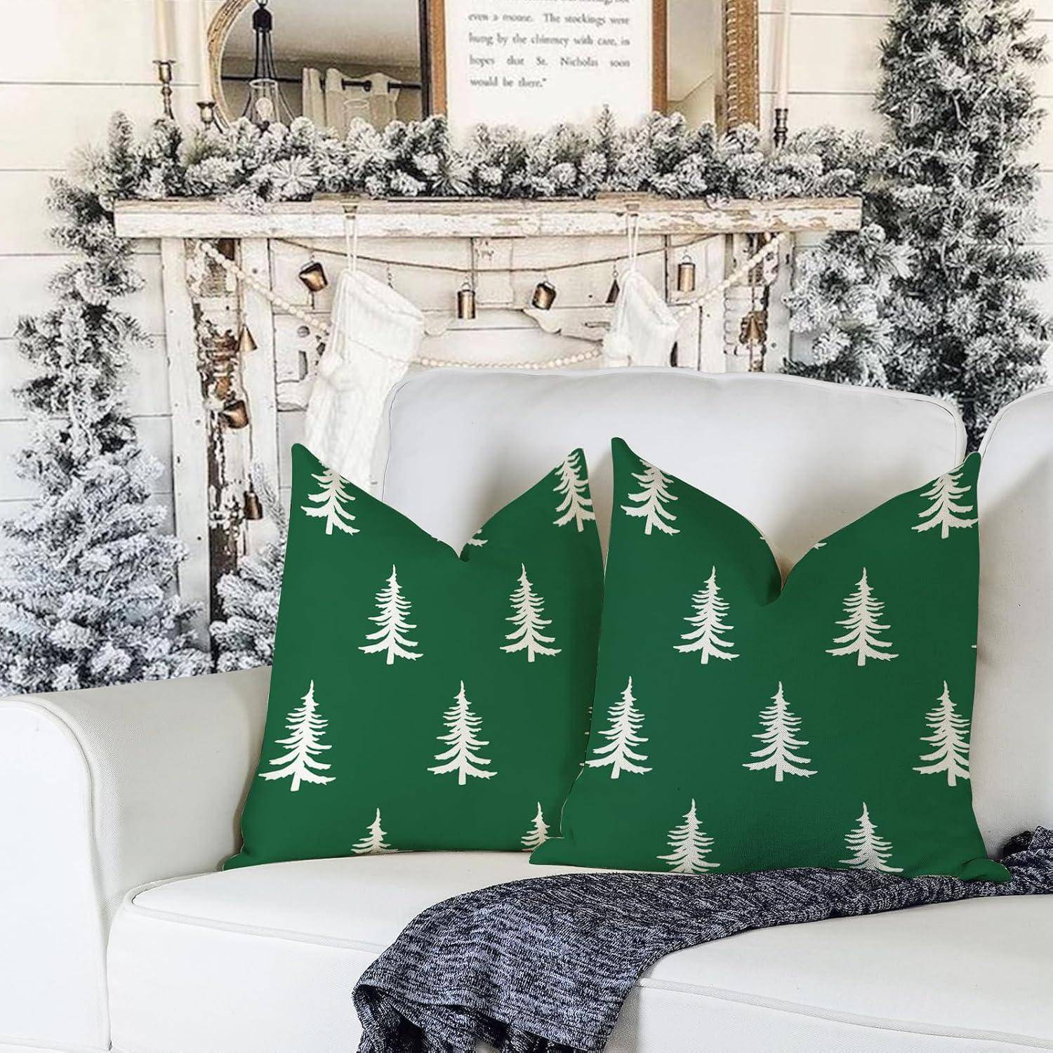 Grüne Kissen mit weißen Kiefernbaum-Drucken auf einem weißen Sofa, platziert vor einem schneebedeckten, weihnachtlich geschmückten Kaminsims mit Weihnachtsstrümpfen.