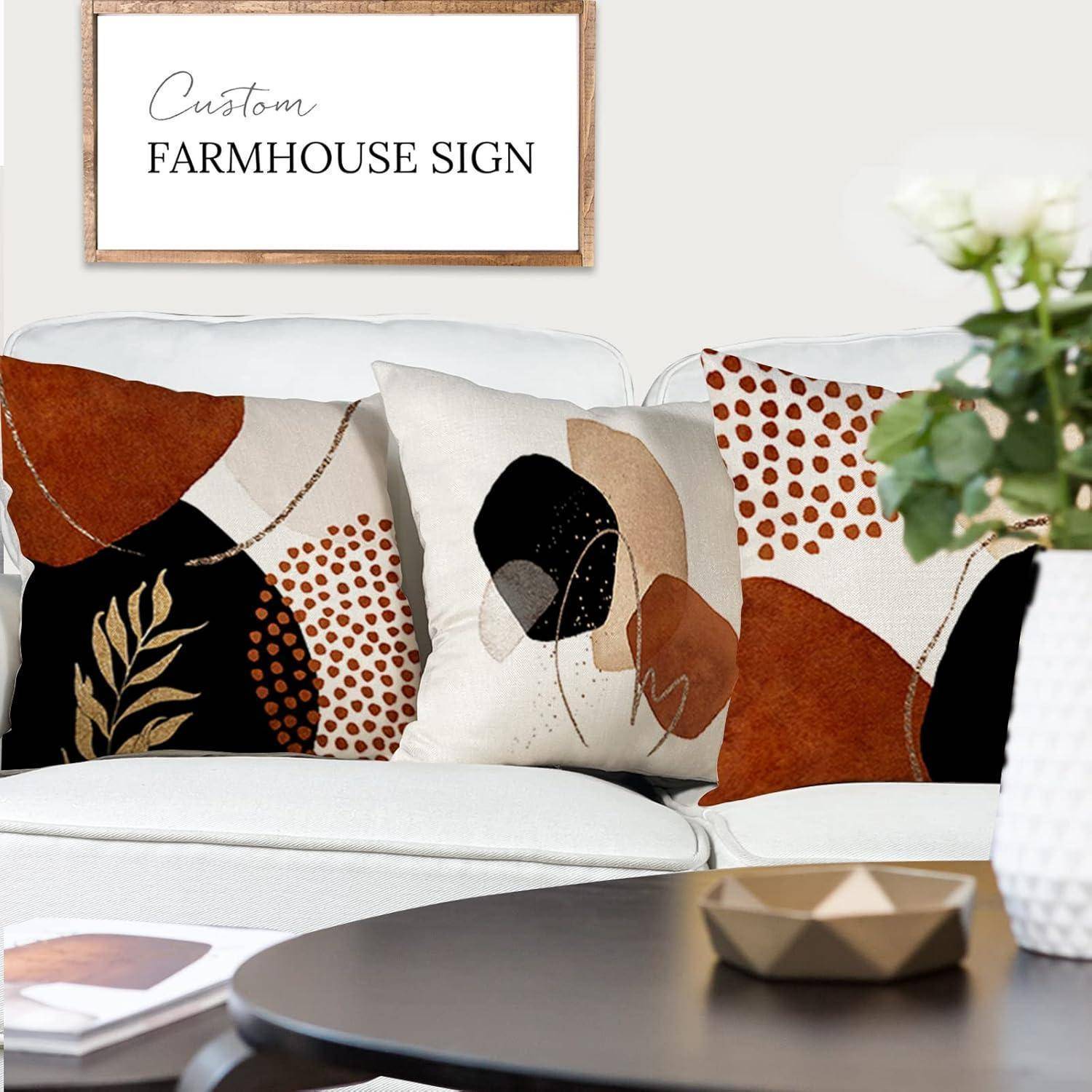 Ein weißes Sofa mit drei abstrakten, gemusterten Kissen. Darüber hängt ein gerahmtes Schild mit der Aufschrift „Custom Farmhouse Sign
