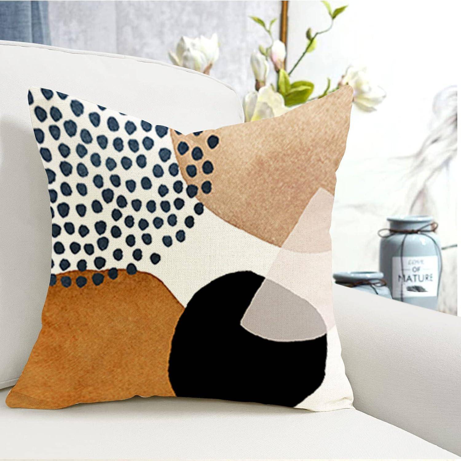 Ein dekorativer Kissenbezug mit abstrakten geometrischen Mustern in Schwarz, Weiß, Beige und Braun liegt auf einem weißen Sofa mit unscharfem Hintergrund.
