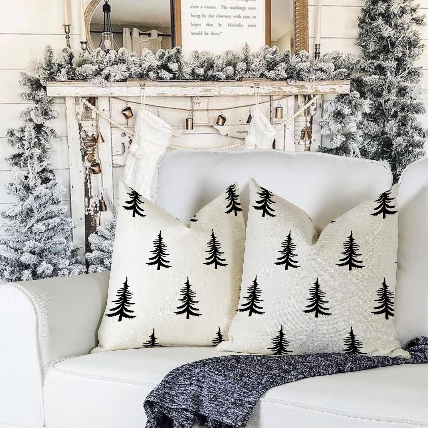 Drei dekorative Kissen mit schwarzen Baummotiven auf einem weißen Sofa, vor einem weißen, schneebedeckten Kamin mit Weihnachtsstrümpfen.