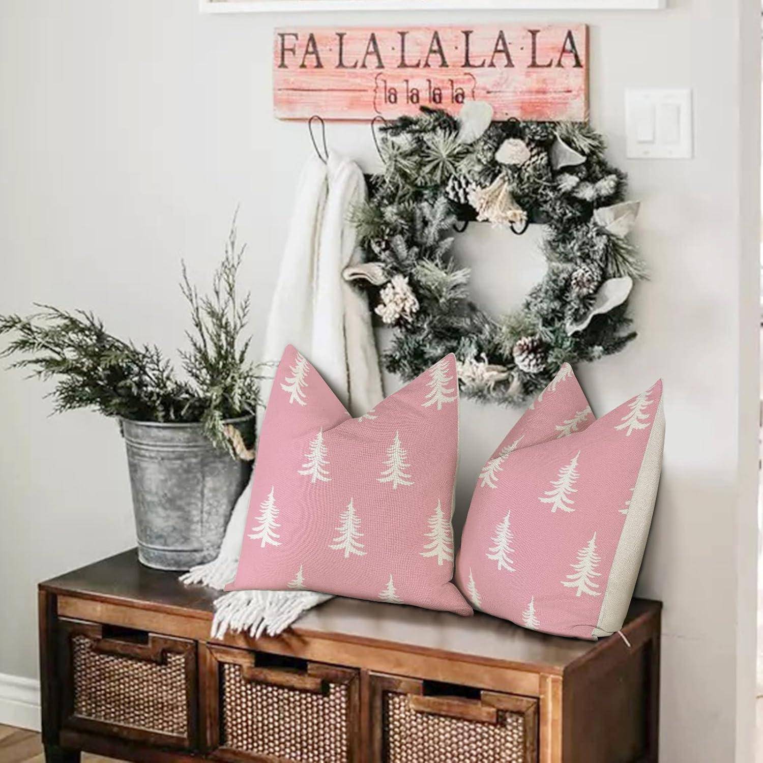 Festlicher Raum mit einem Kranz an der Wand, einem Schild mit der Aufschrift ‚Fa La La La' und zwei rosa Kissenbezügen mit Baummustern auf einer Holzbank.