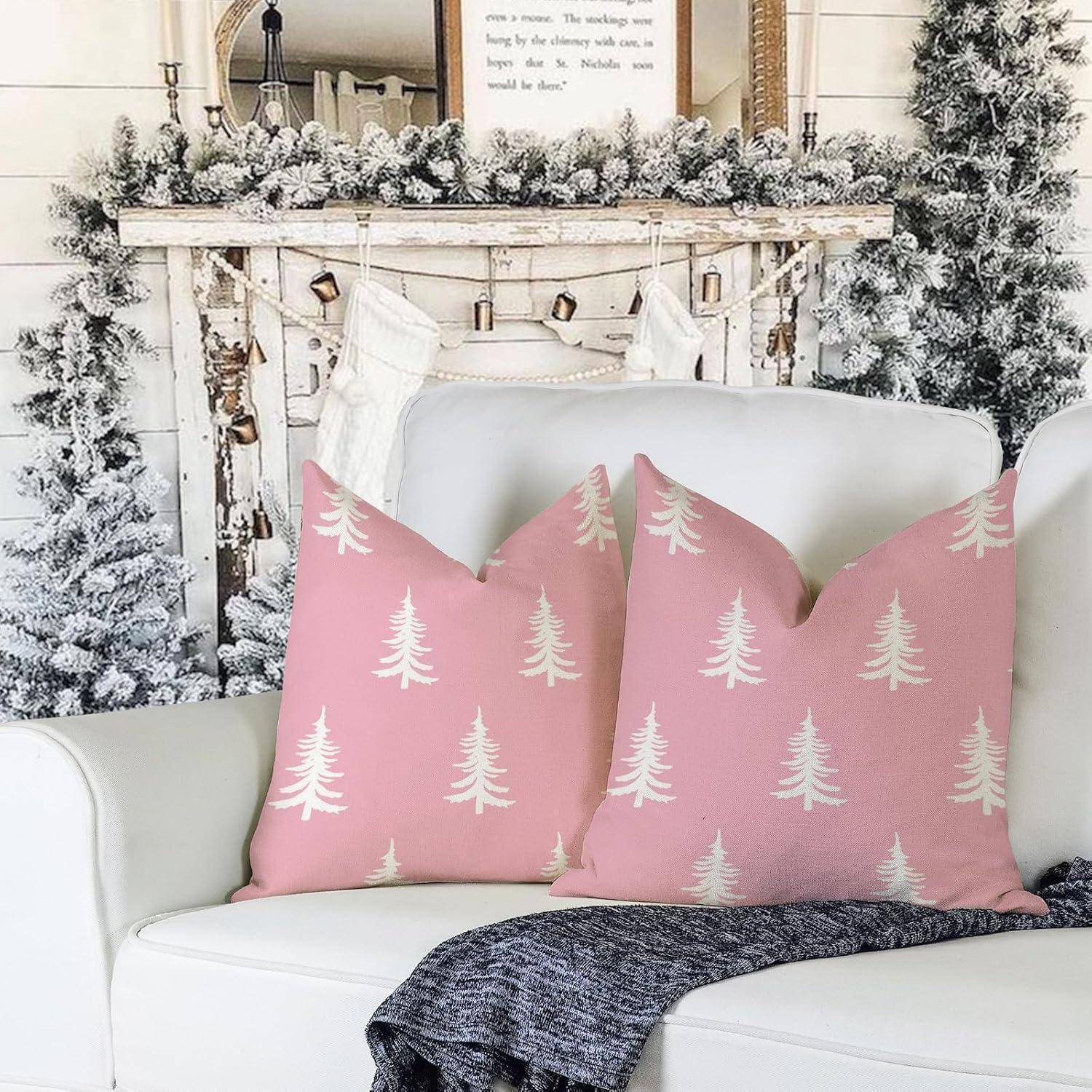 Ein gemütliches Wohnzimmer mit einem weißen Sofa, geschmückt mit rosa Kissen, die weiße Kiefernbaumzeichnungen tragen. Ein weißer verschneiter Kaminsims mit Weihnachtsstrümpfen hängt im Hintergrund.