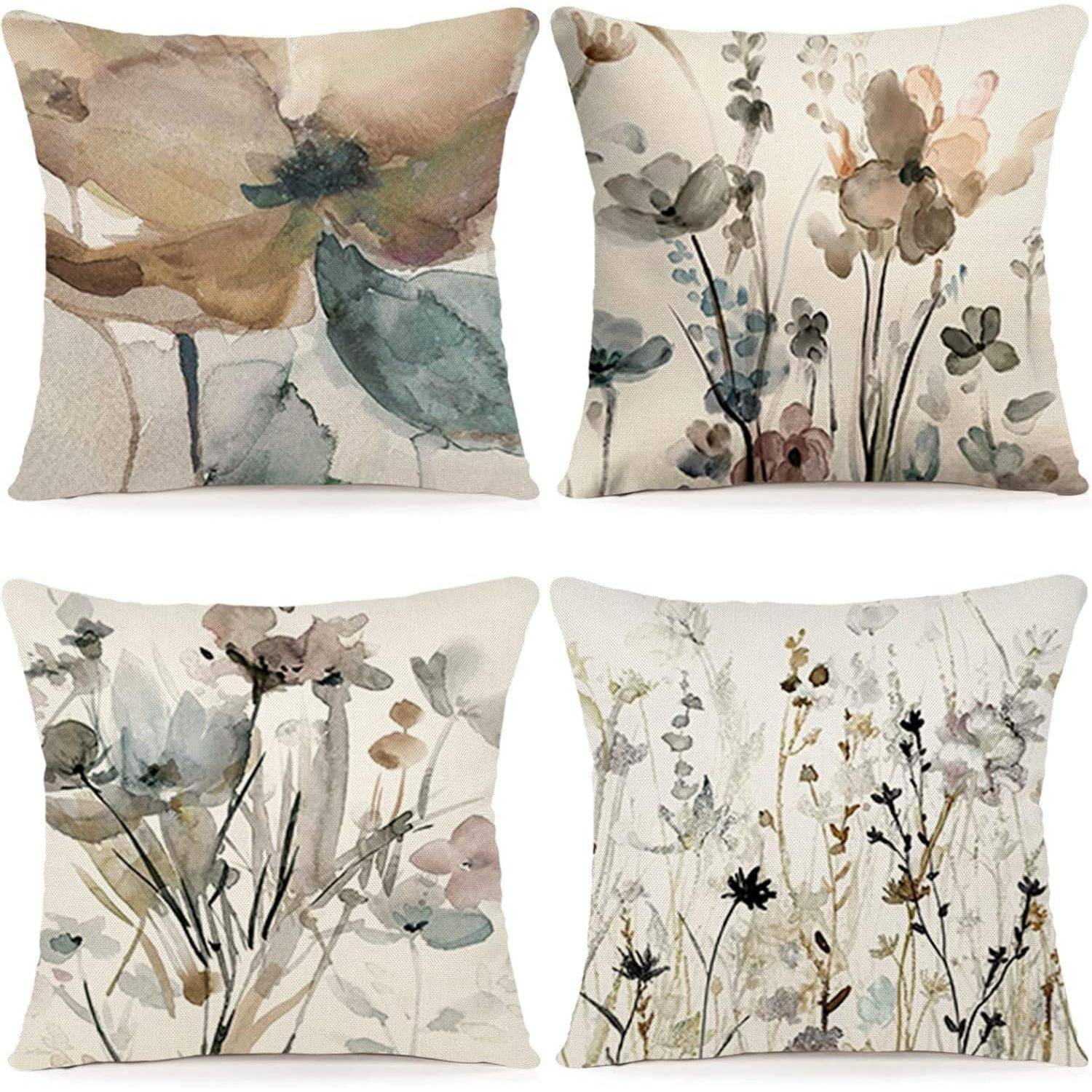 Vier dekorative Kissen zeigen Aquarell-Blumendesigns in weichen, gedämpften Farben und präsentieren abstrakte Blumen und Blätter.
