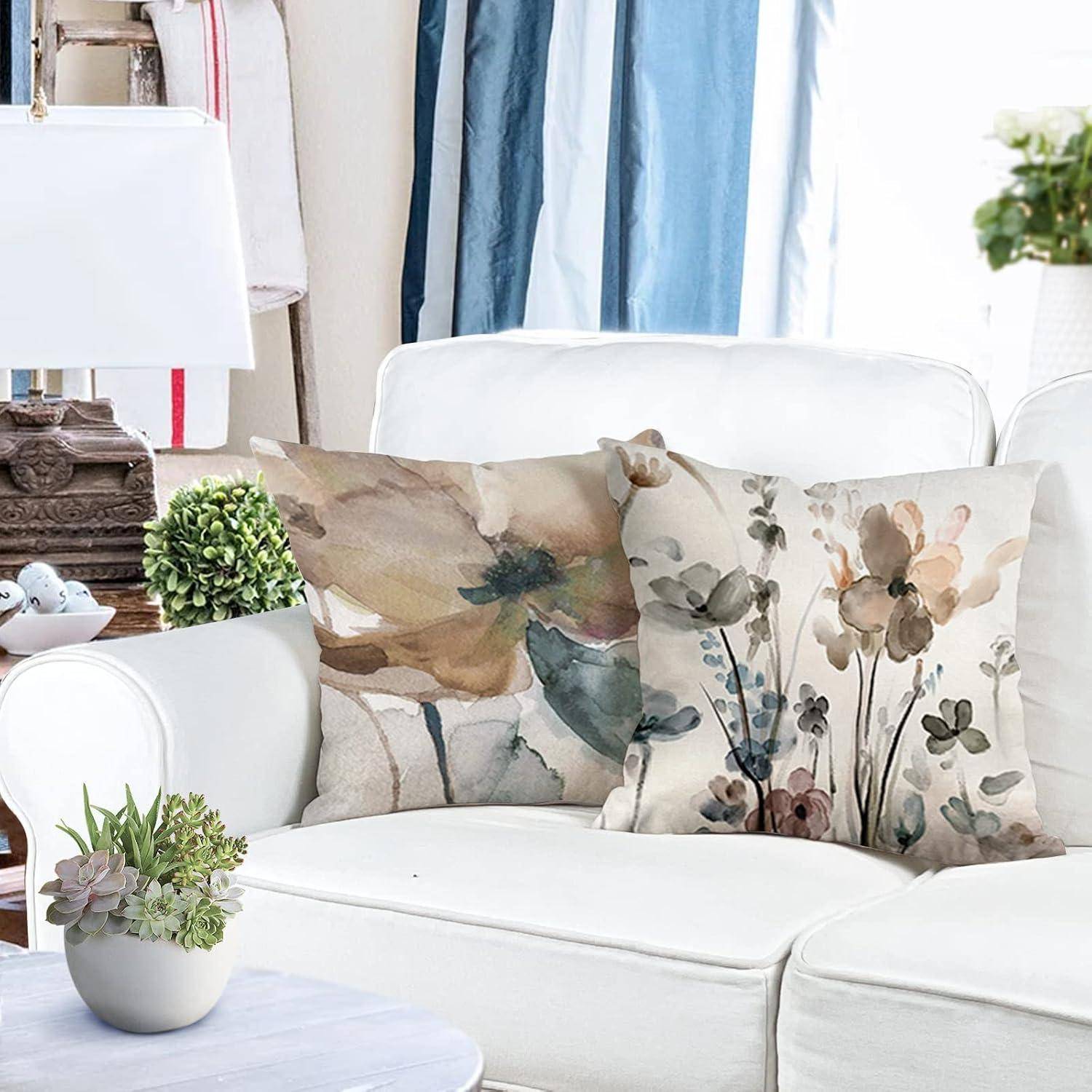 Ein weißes Sofa mit Kissen im Blumenmuster in einem hellen Raum mit blauen und beigen Vorhängen; eine weiße Lampe und Pflanzen ergänzen die Dekoration.