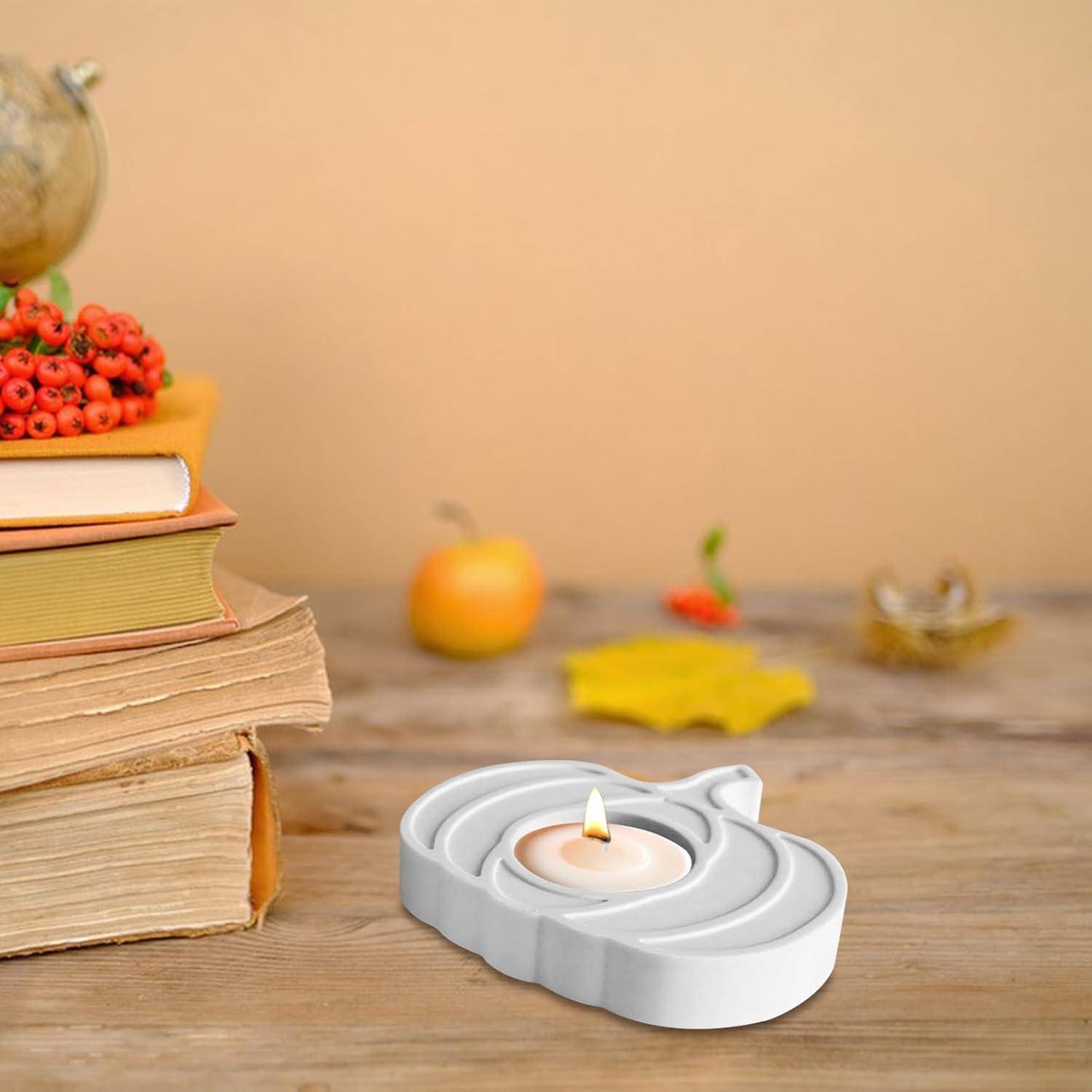 Ein Stapel Bücher mit roten Beeren obenauf steht auf einem Tisch. Eine brennende Kerze in einem weißen Halter befindet sich im Vordergrund, daneben kleine Kürbisse.