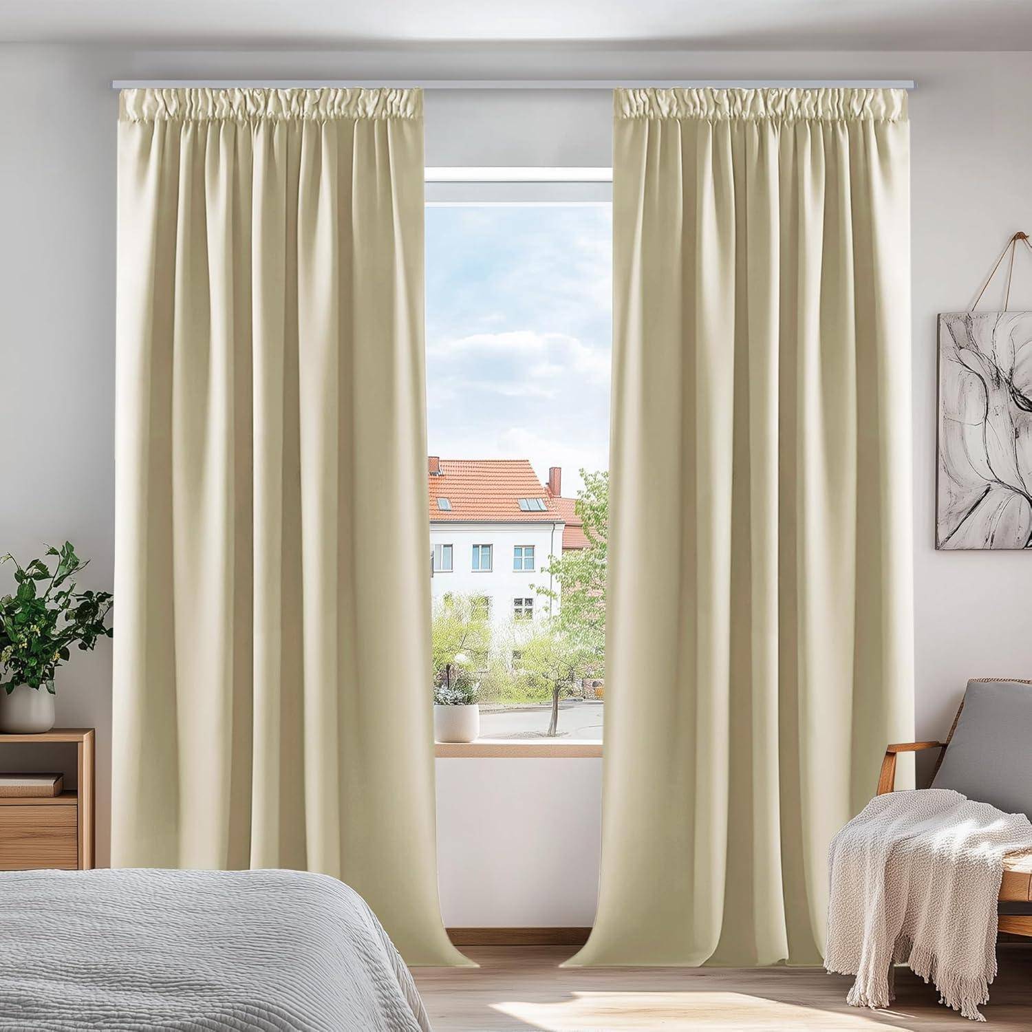 Ein Schlafzimmer mit cremefarbenen Vorhängen, Blick aus dem Fenster auf Gebäude, ein Bett mit einer Decke, eine Pflanze auf dem Nachttisch und einem gerahmten Kunstwerk an der Wand.