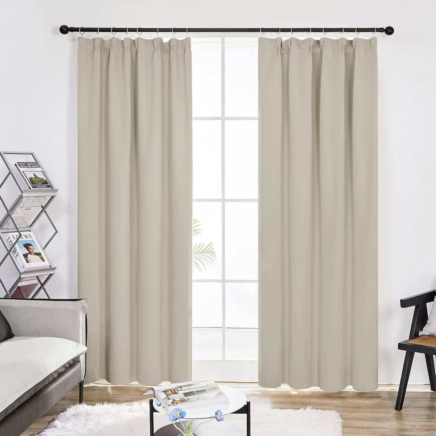 Ein Wohnzimmer mit beigen Vorhängen an einem großen Fenster, einem grauen Sofa, einem kleinen Tisch und einem Stuhl, der eine gemütliche und minimalistische Atmosphäre schafft.