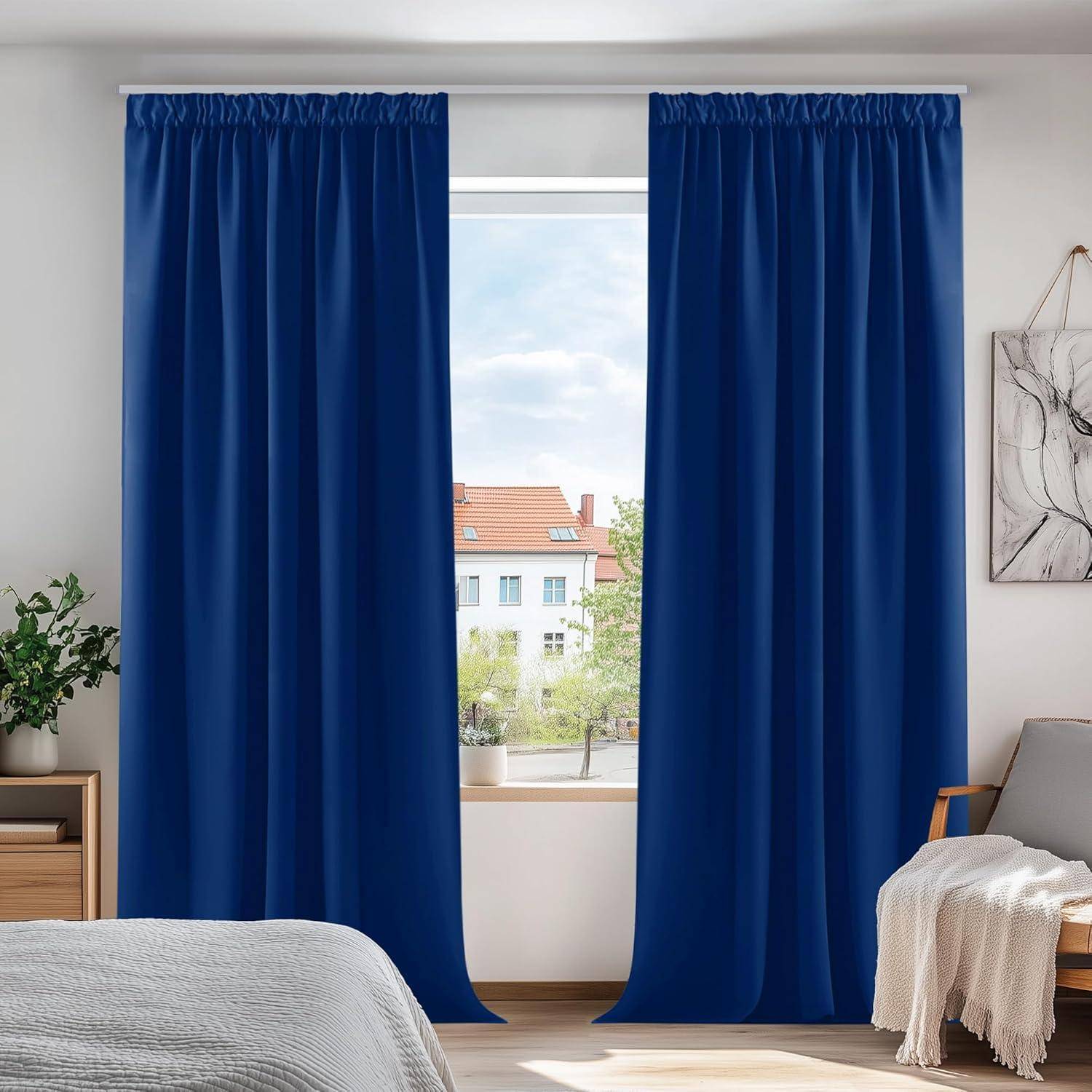 Ein Schlafzimmer zeigt blaue Vorhänge, die ein Fenster mit Blick auf Gebäude und Bäume umrahmen. Ein Bett und Kunstwerke sind teilweise sichtbar.