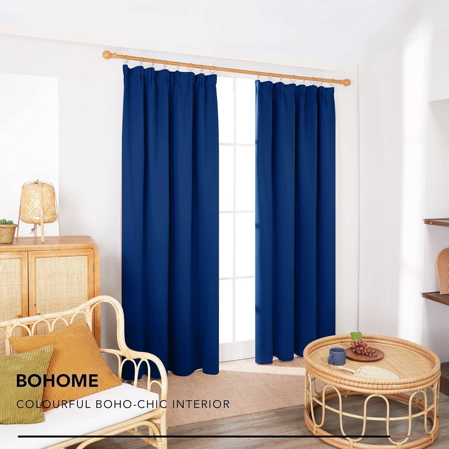Ein Raum mit blauen Vorhängen an einem weißen Fenster, einem Korbstuhl, einem Holztisch mit einer Lampe und dem Text 