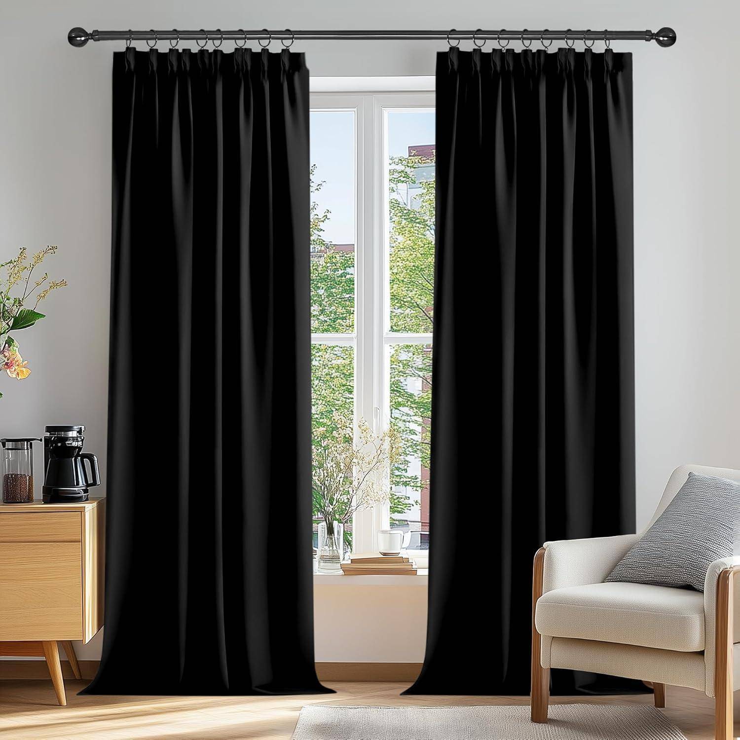 Ein großes Fenster, gesäumt von schwarzen Vorhängen, lässt helles Licht herein und beleuchtet einen gemütlichen Raum mit einem beigen Sessel und einem Holzschrank.