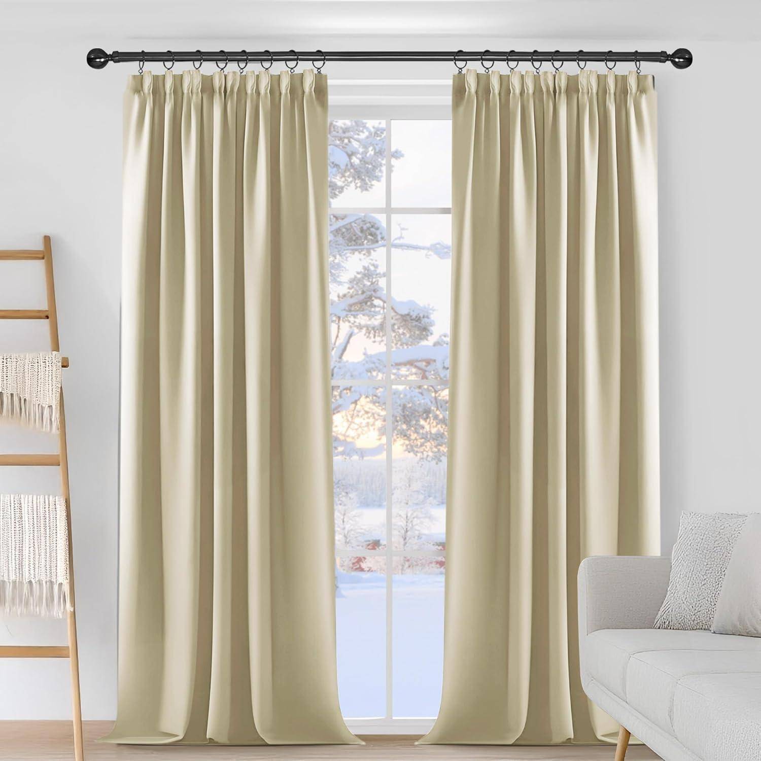 Beige Vorhänge hängen an einer Stange in einem Wohnzimmer, wobei ein Fenster eine verschneite Außenszene offenbart. Ein weißes Sofa und eine Deckenleiter befinden sich in der Nähe.