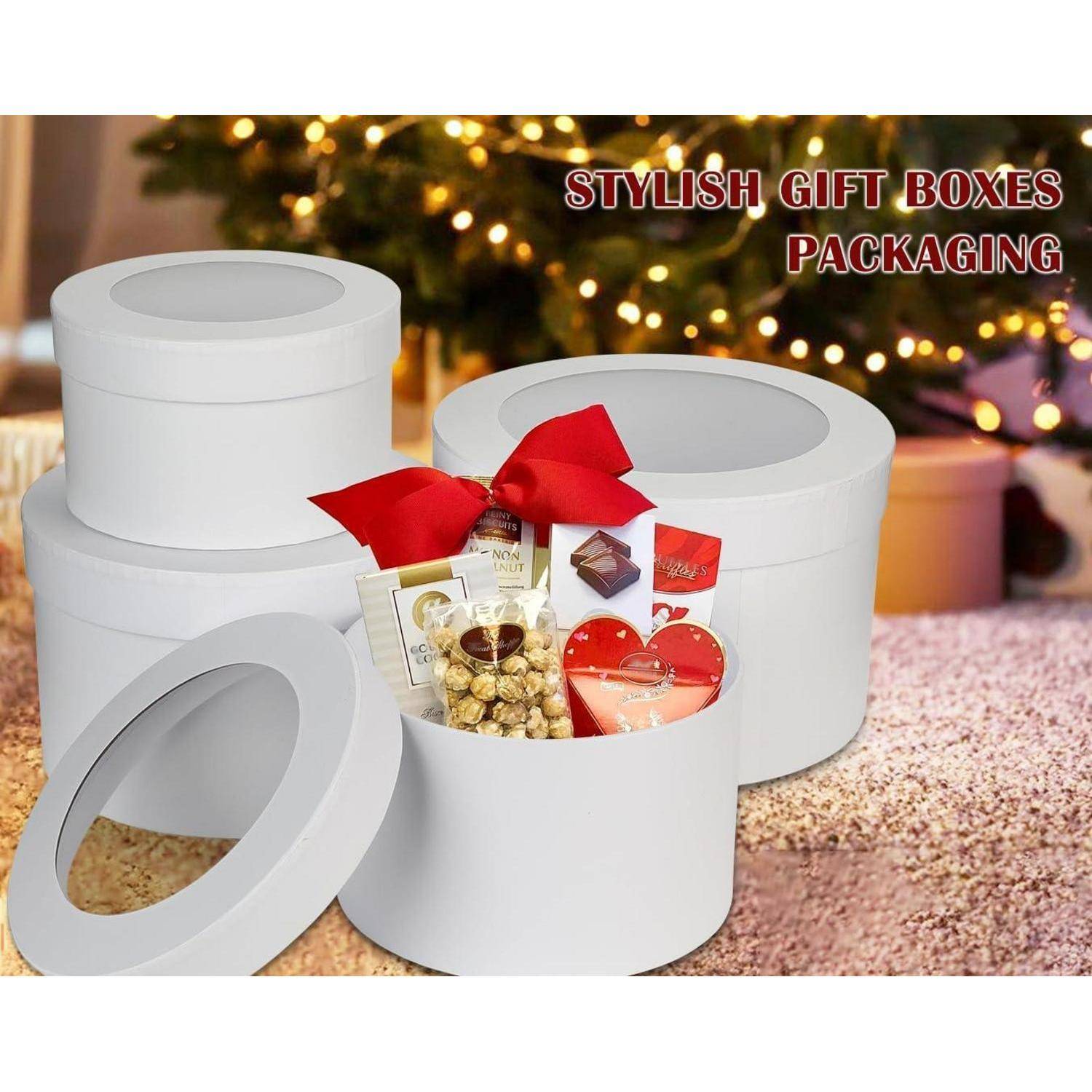 Runde weiße Geschenkboxen mit Deckeln, gefüllt mit Snacks und einer roten Schleife, vor einem beleuchteten Weihnachtsbaum. Text: 'Stilvolle Geschenkbox-Verpackung'.