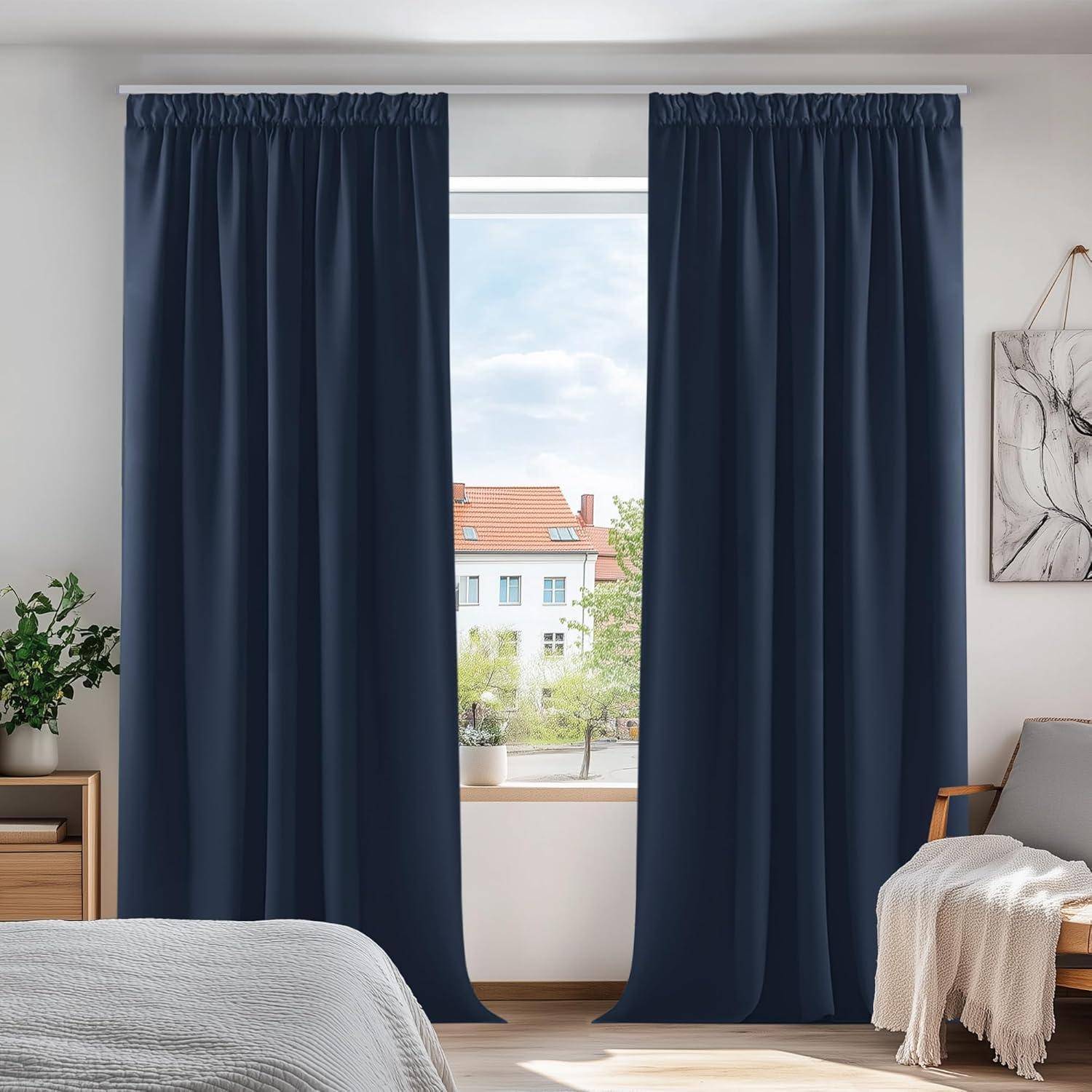 Ein heller Raum mit dunkelblau gerahmten Vorhängen, die ein Fenster umgeben, durch das ein Blick auf Bäume und Gebäude sichtbar ist. Eine Pflanze und ein Sessel befinden sich an den Seiten.
