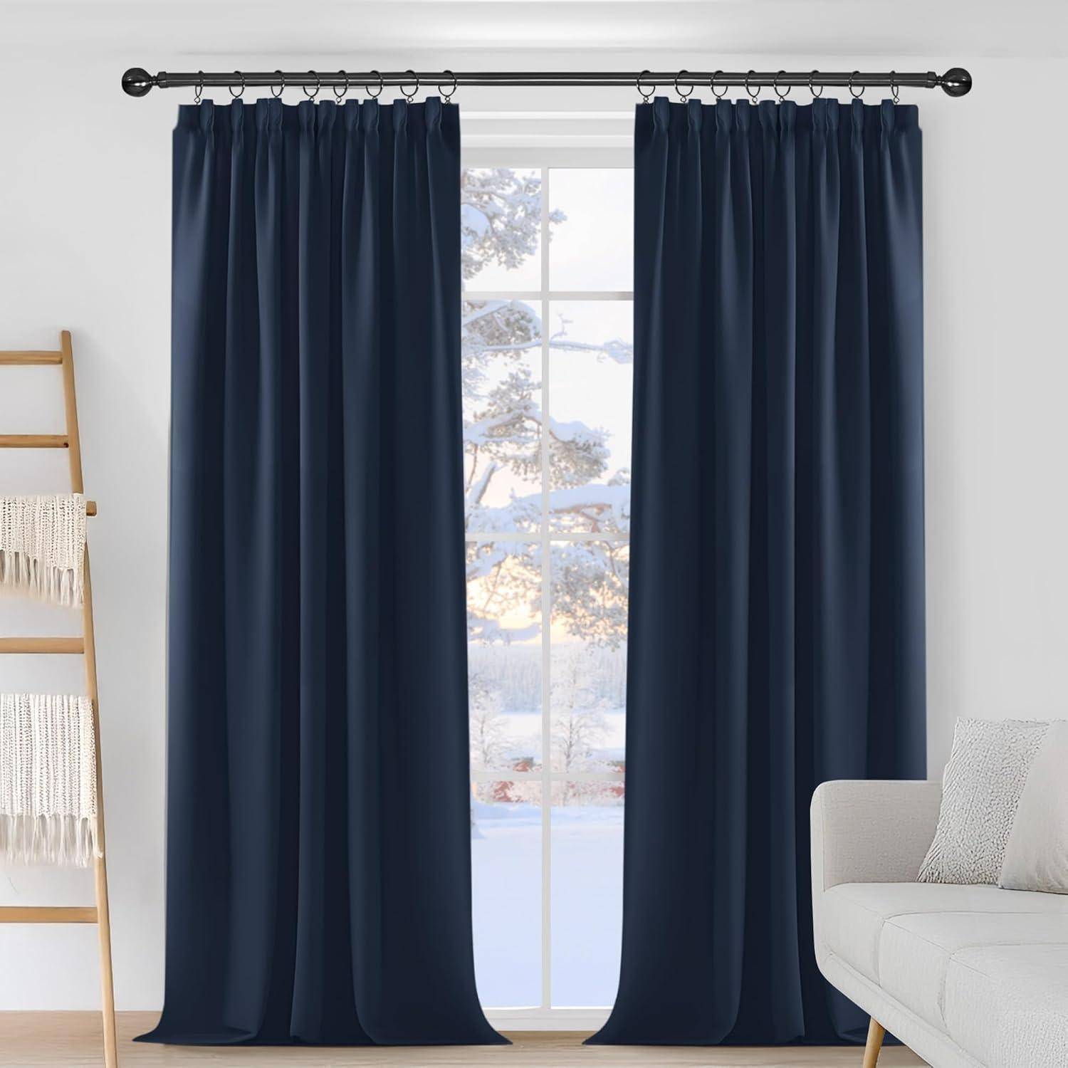Ein Wohnzimmer mit dunkelblau-farbenen Vorhängen, einem hellgefärbten Sofa und einer Holzleiter, auf der eine beige Decke hängt. Eine verschneite Landschaft ist draußen durchs Fenster zu sehen.