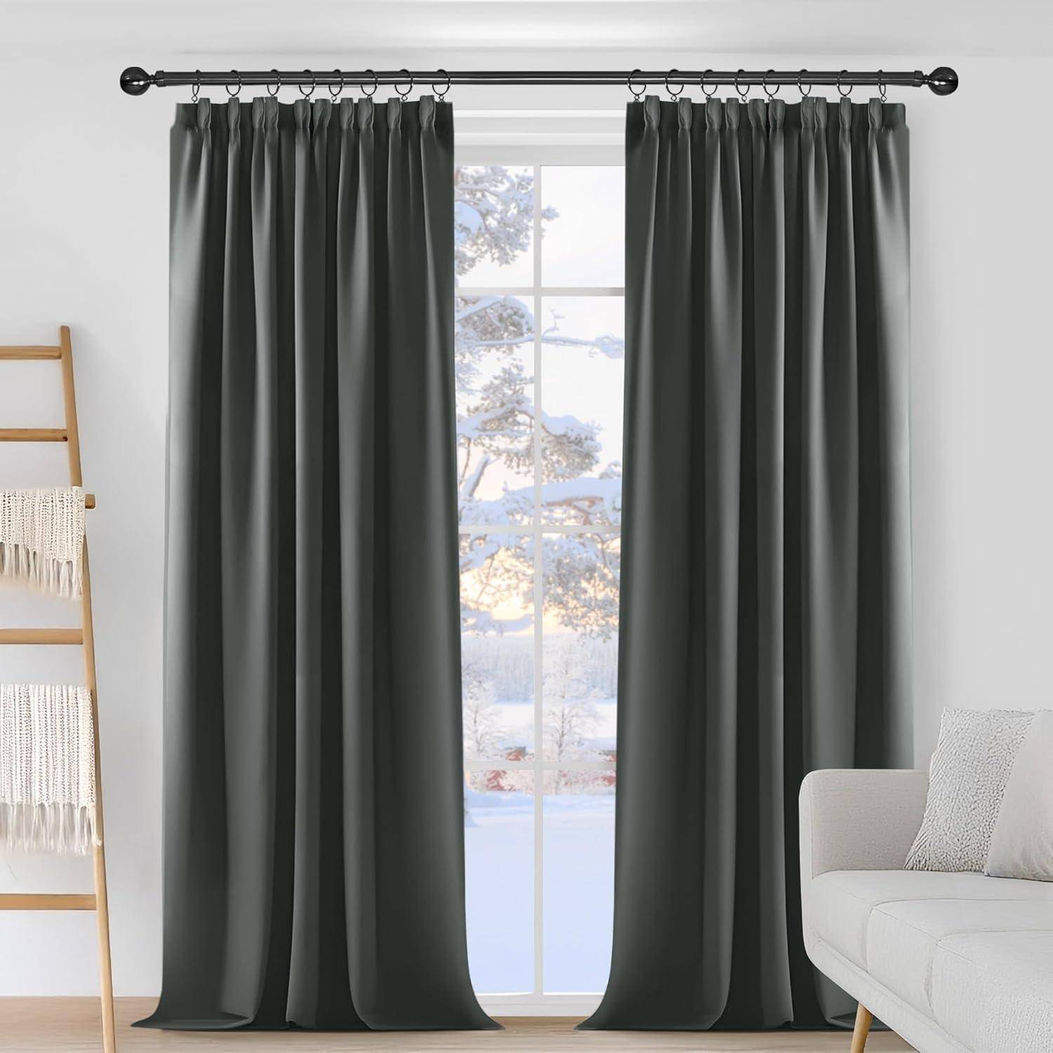 Graue Vorhänge hängen an einem Fenster, hinter dem eine verschneite Landschaft zu sehen ist. Ein weißes Sofa und eine Holzleiter mit einer Decke befinden sich im Raum.