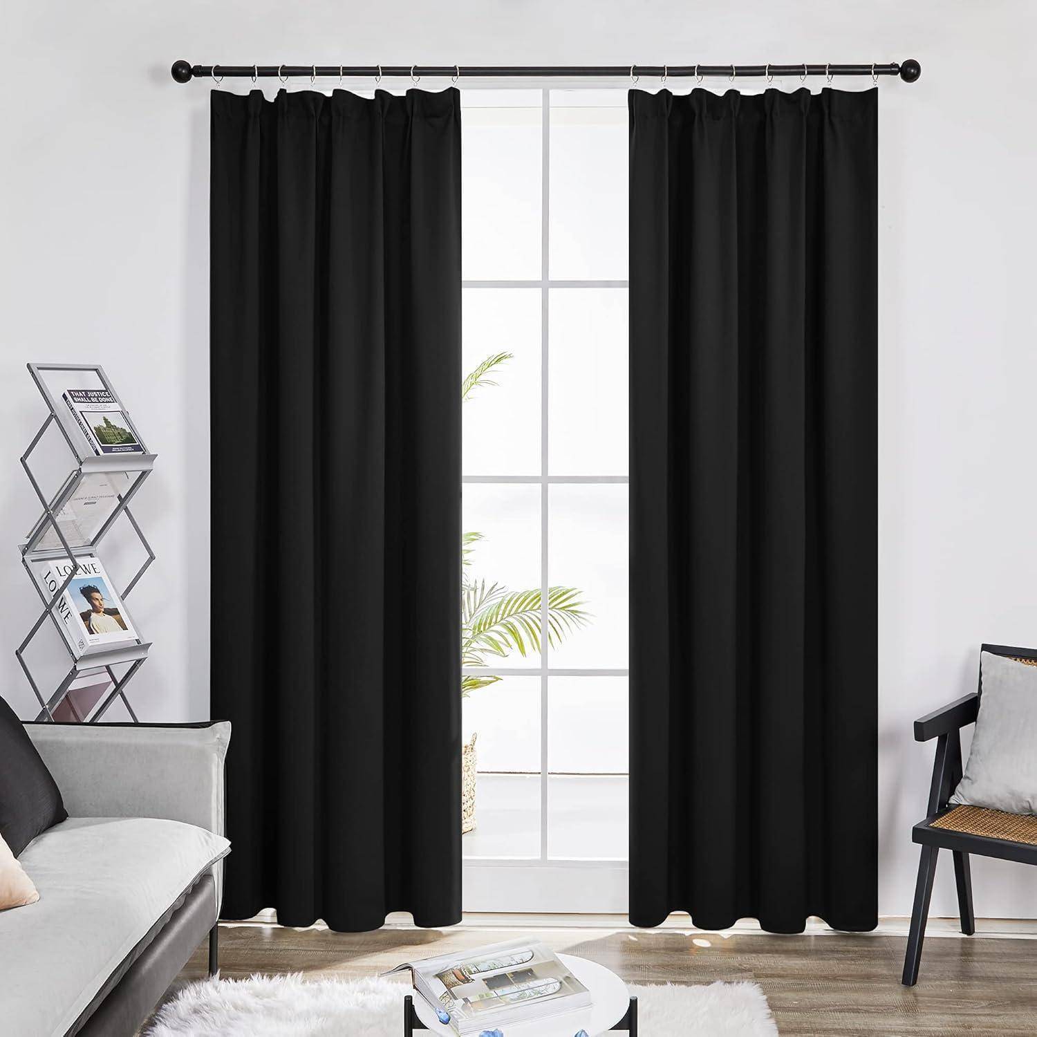 Ein Raum mit einem großen Fenster, das mit schwarzen Vorhängen verhängt ist, ein weißes Sofa links und ein schwarzer Stuhl rechts. Eine Pflanze ist draußen zu sehen.