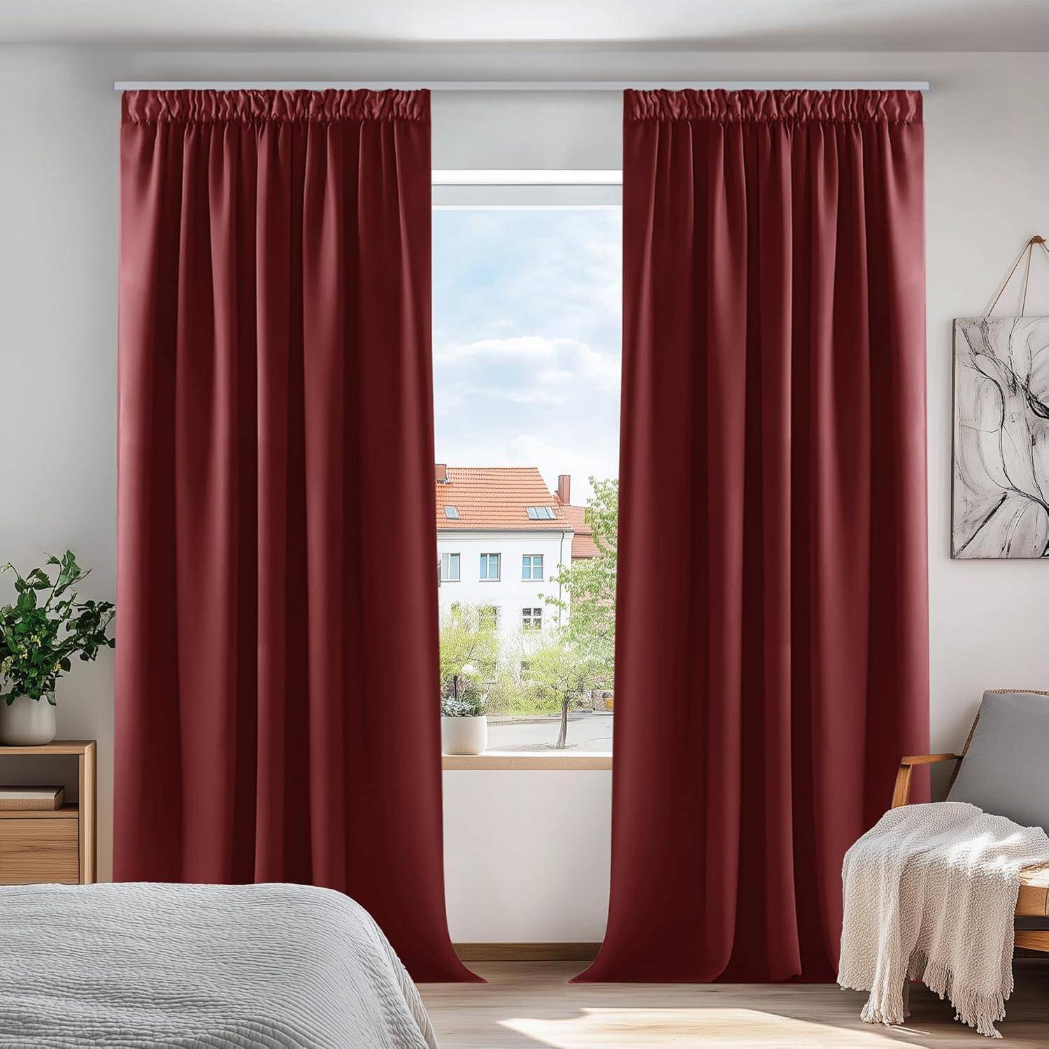 Rote Vorhänge hängen an einem Fenster mit Blick auf Gebäude und Bäume. Ein Bett und ein Stuhl sind teilweise sichtbar und schaffen eine gemütliche Schlafzimmerszene.