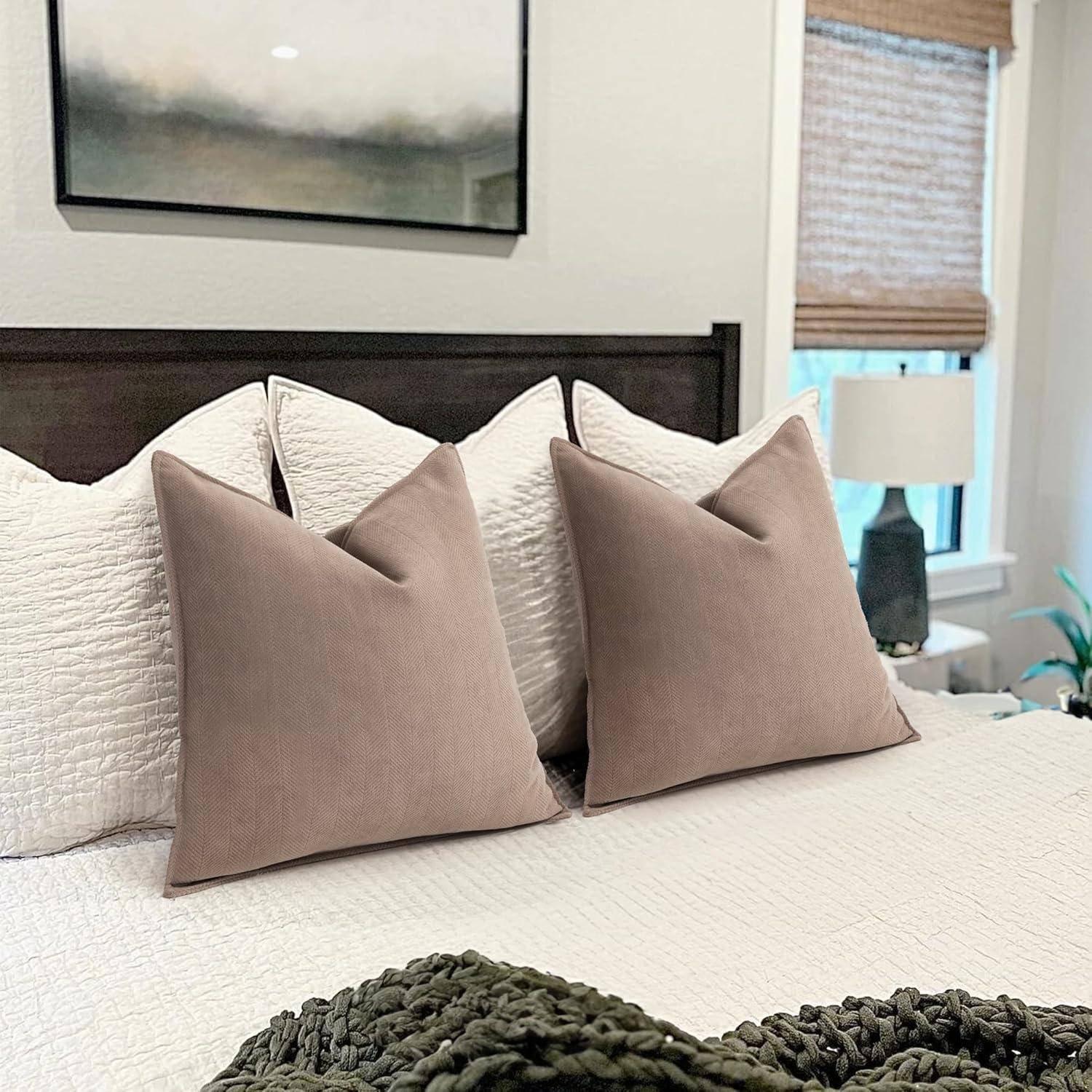 Ein sauber gemachtes Bett mit einem dunklen Holzkopfteil zeigt vier große Kissen - zwei weiße und zwei beige - vor einem unscharfen Wandbild und einer Lampe.