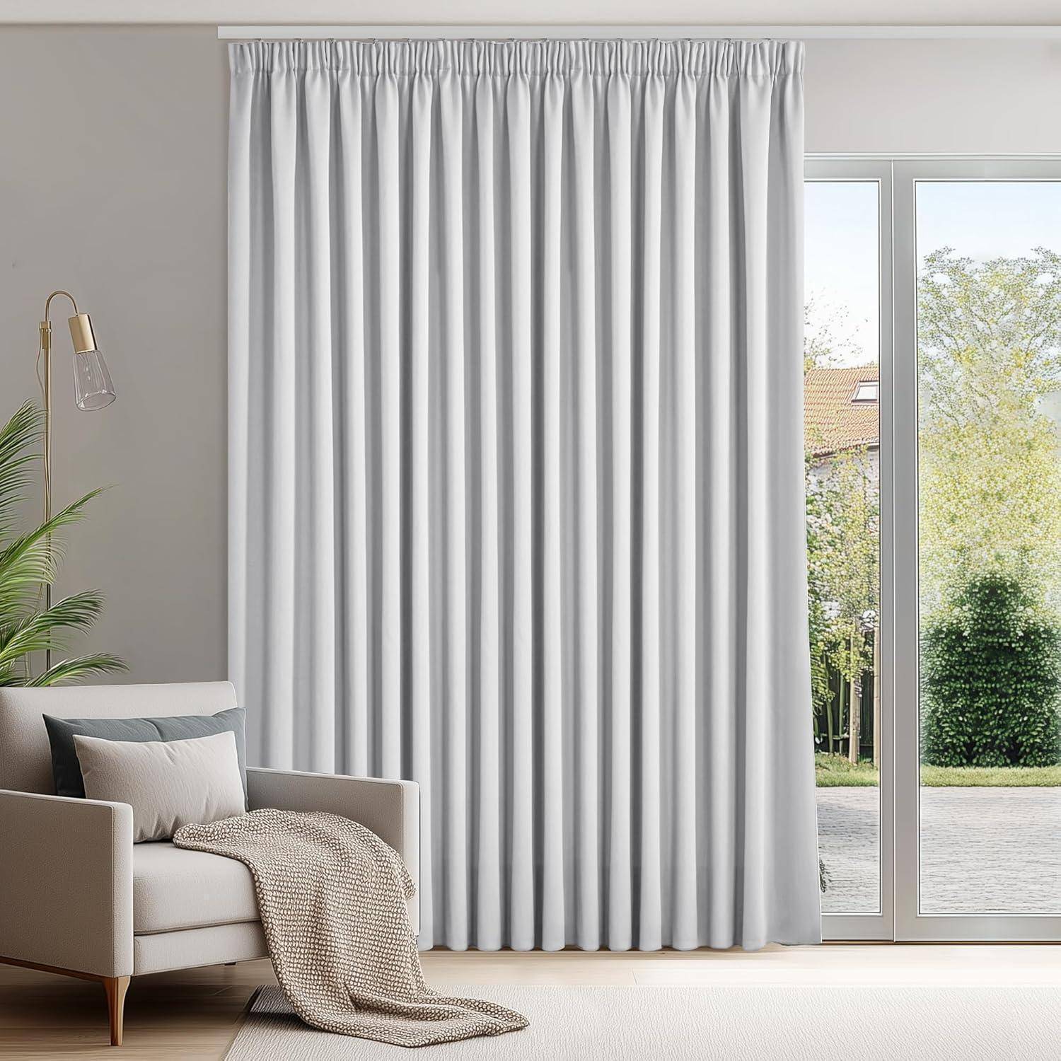 Ein Wohnzimmer mit einem beigen Sofa, einem weißen Vorhang und einer hohen Stehlampe neben einem großen Fenster, das einen Blick in den Garten nach draußen freigibt.