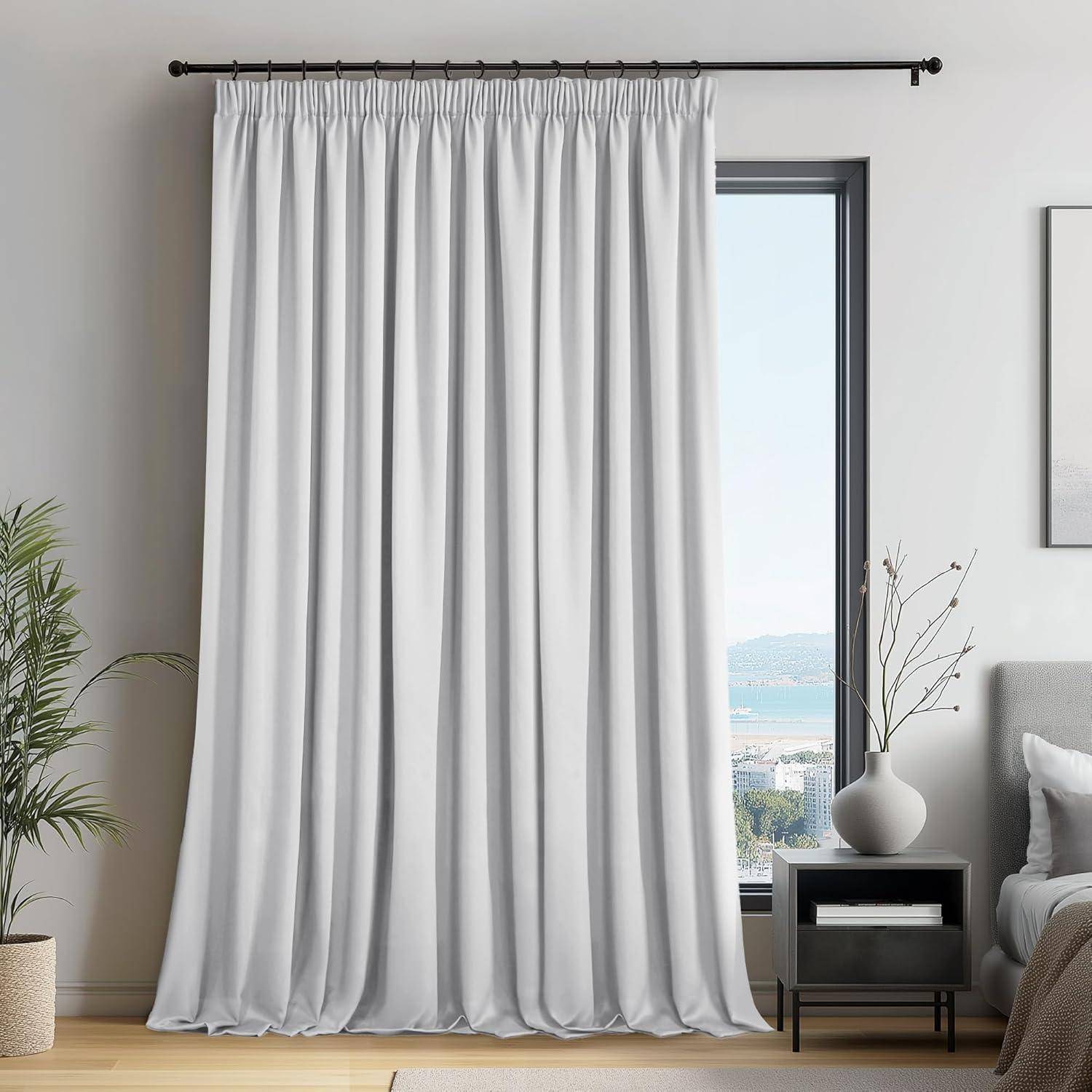 Weiße bodenlange Vorhänge hängen neben einem Fenster, das einen Blick auf die Küste freigibt. Ein kleiner Tisch mit einer Vase steht in der Nähe in einem minimalistischen Wohnzimmer.