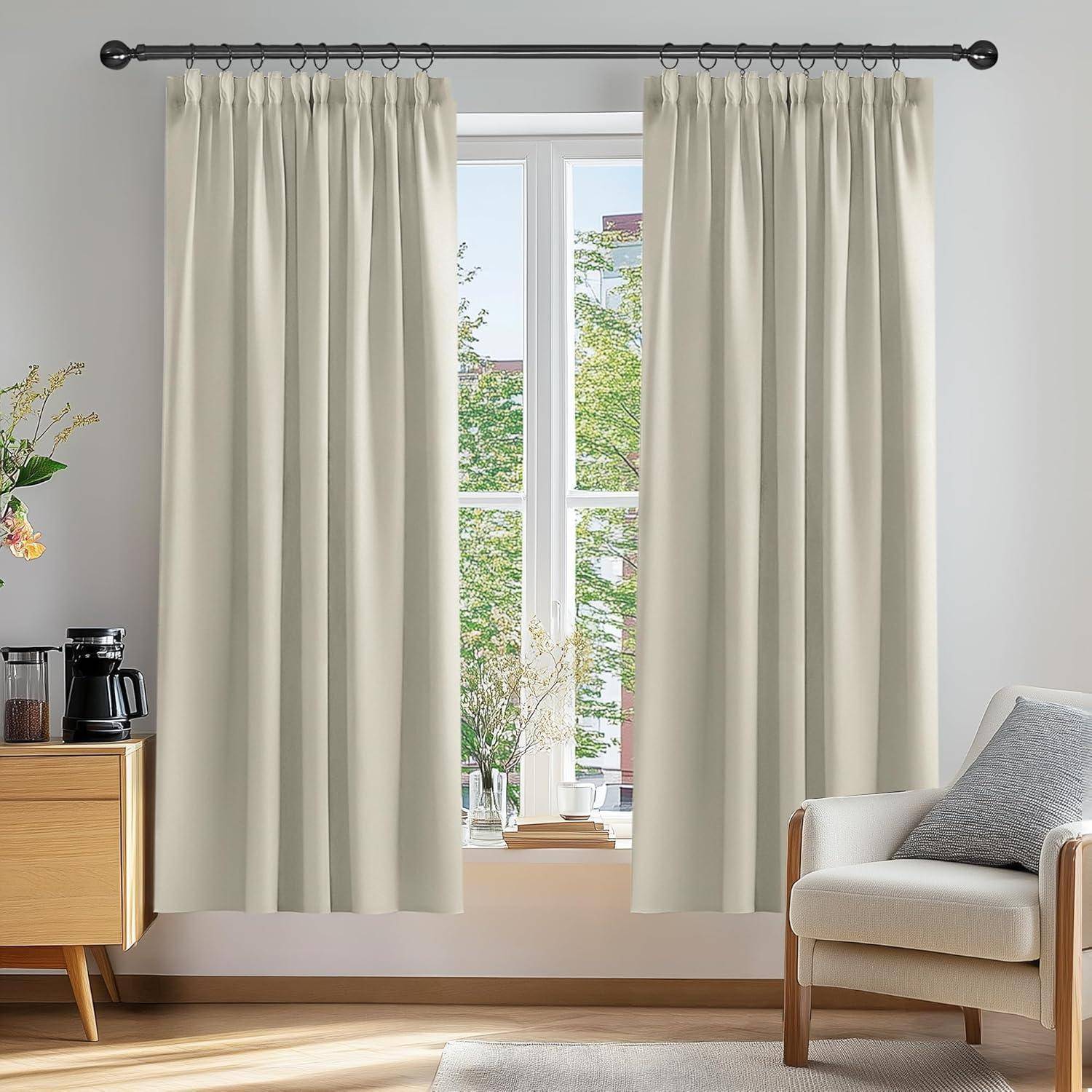 Wohnzimmer mit beigen Vorhängen, zentriertem Fenster mit Blick auf grüne Außenanlage, flankiert von einem Holzschrank mit einer Kaffeemaschine und einem gepolsterten Sessel.