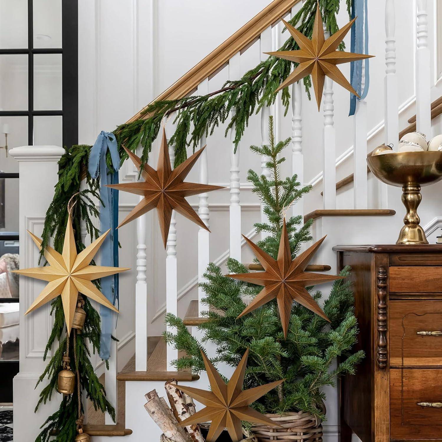 Treppe, geschmückt mit grüner Girlande, goldenen Sternen und Bändern, neben einer Holztruhe mit einem kleinen Topfbaum und goldenem Kerzenhalter.