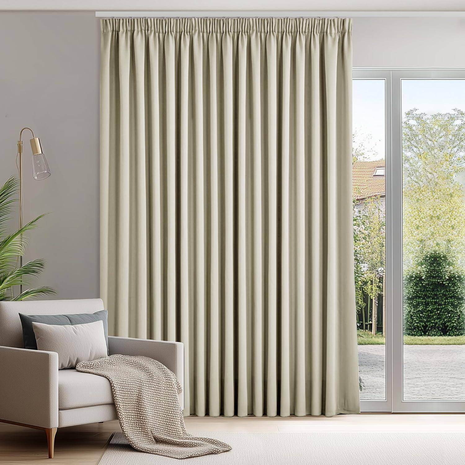 Ein gemütliches Wohnzimmer zeigt ein beiges Sofa mit einer grauen Decke und einem Kissen, daneben eine Stehlampe und ein großes Fenster mit geschlossenen cremefarbenen Vorhängen.