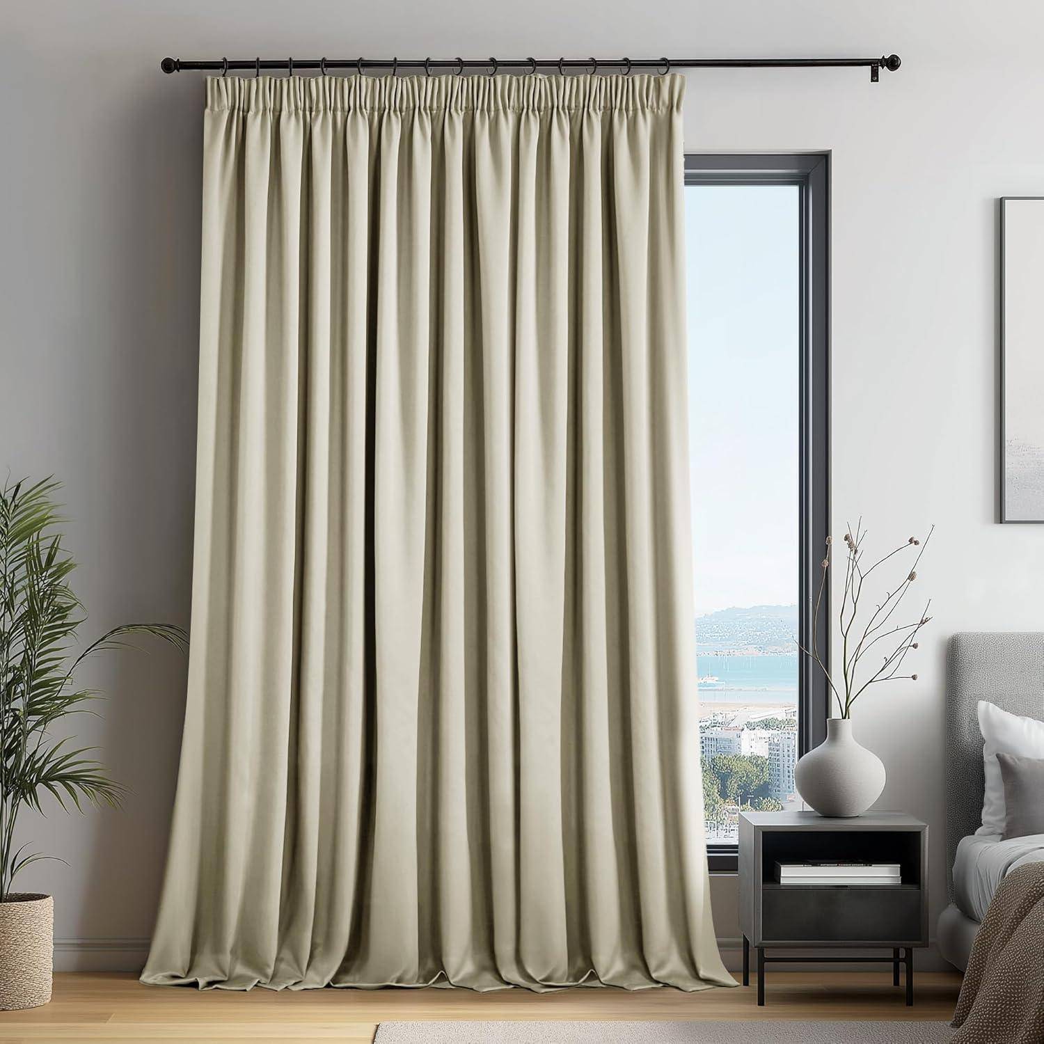 Ein hoher, beiger Vorhang verdeckt ein Fenster mit einer malerischen Meeresaussicht. Eine weiße Vase mit Zweigen steht auf einem Beistelltisch neben einem grauen Sofa.