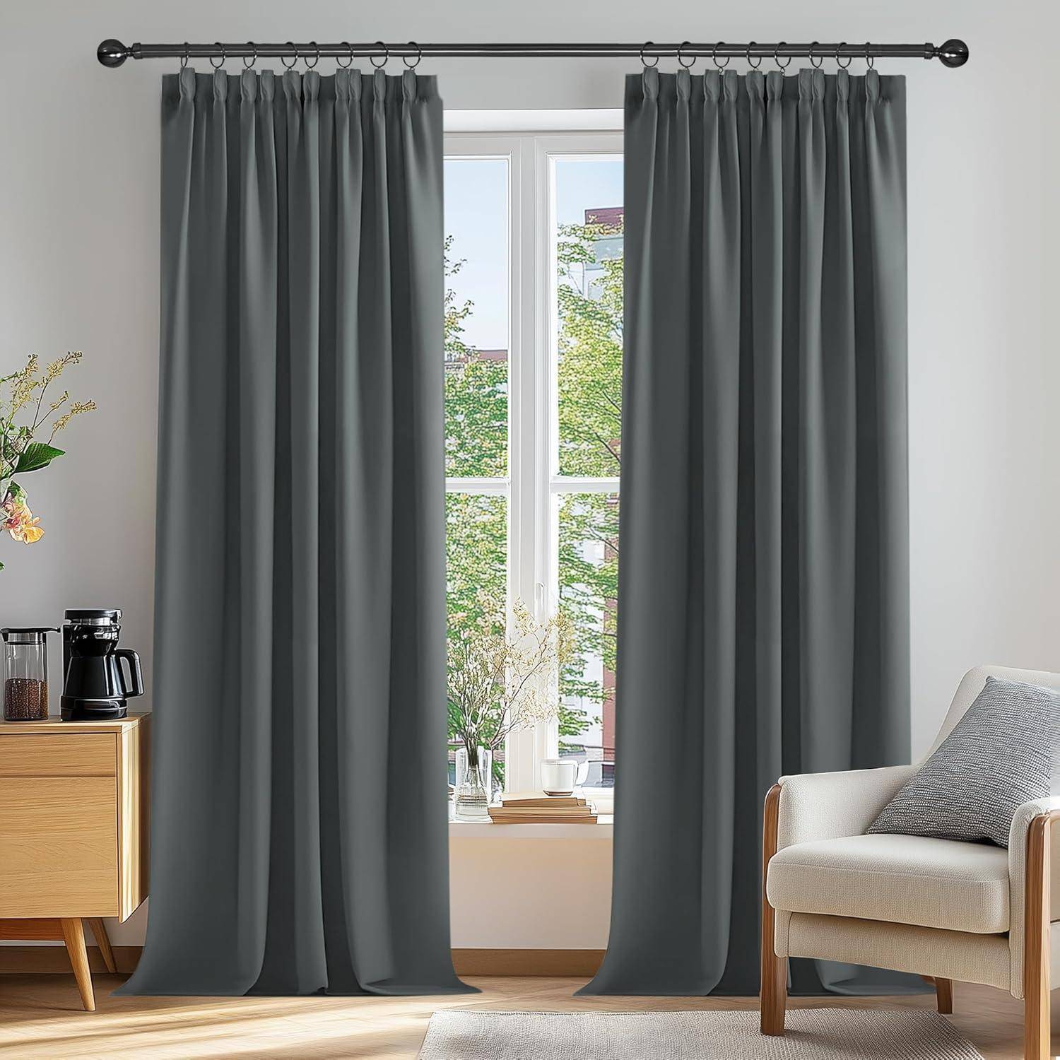 Ein Wohnzimmer mit grauen Vorhängen, einem beigen Sessel, einem Holzseitentisch mit einer Kaffeemaschine und einem Fenster, das einen Blick auf Bäume freigibt.