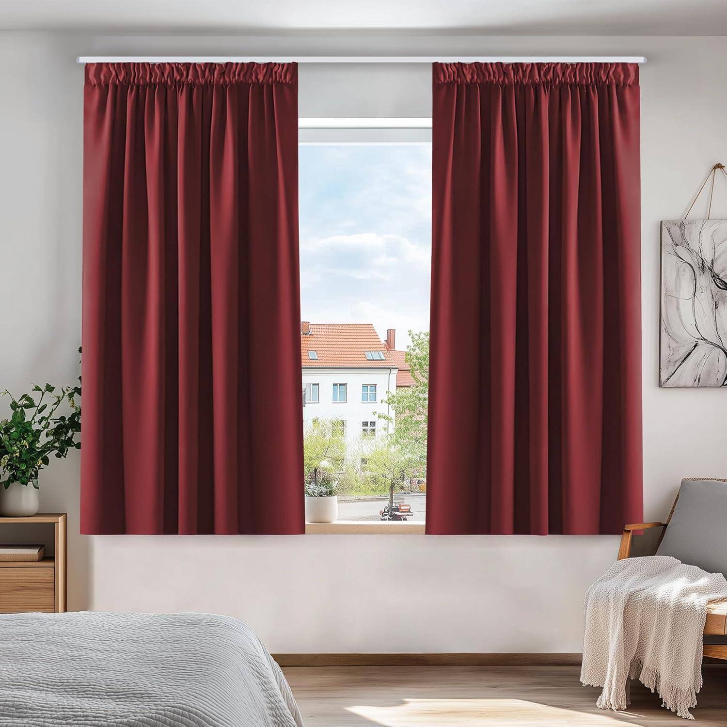 Ein Fenster mit roten Vorhängen bietet einen sonnigen Blick auf einige Wohngebäude. Eine Pflanze und Kunstwerke sind im Raum zu sehen.