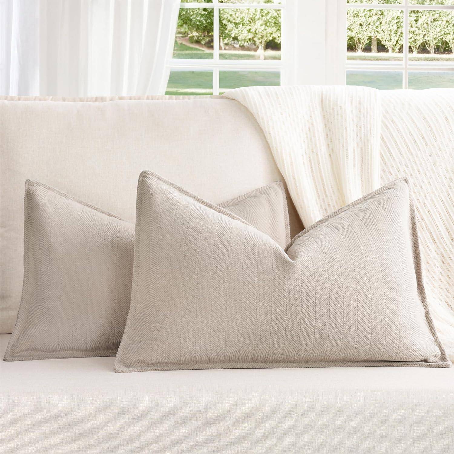 Ein gemütliches Wohnzimmer zeigt ein beige Sofa mit zwei passenden strukturierten Kissen. Eine weiße Strickdecke fällt über die Rückenlehne des Sofas.