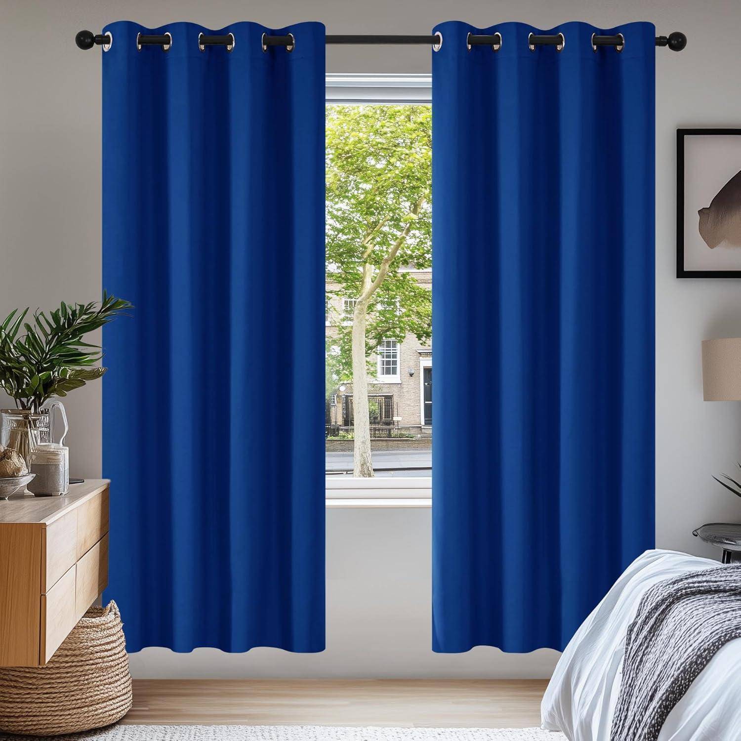 Raum mit hellblauen Vorhängen, Blick auf grüne Bäume draußen am Fenster und modernem Mobiliar, darunter ein Holzseitentisch und gerahmte Kunstwerke.