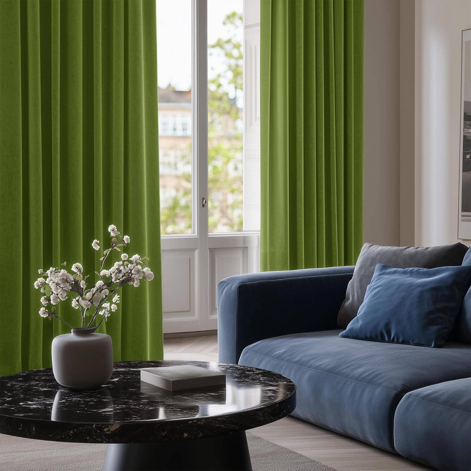 Ein modernes Wohnzimmer mit einem blauen Sofa, grünen Vorhängen und einem runden schwarzen Marmortisch. Eine Vase mit weißen Blumen steht auf dem Tisch.