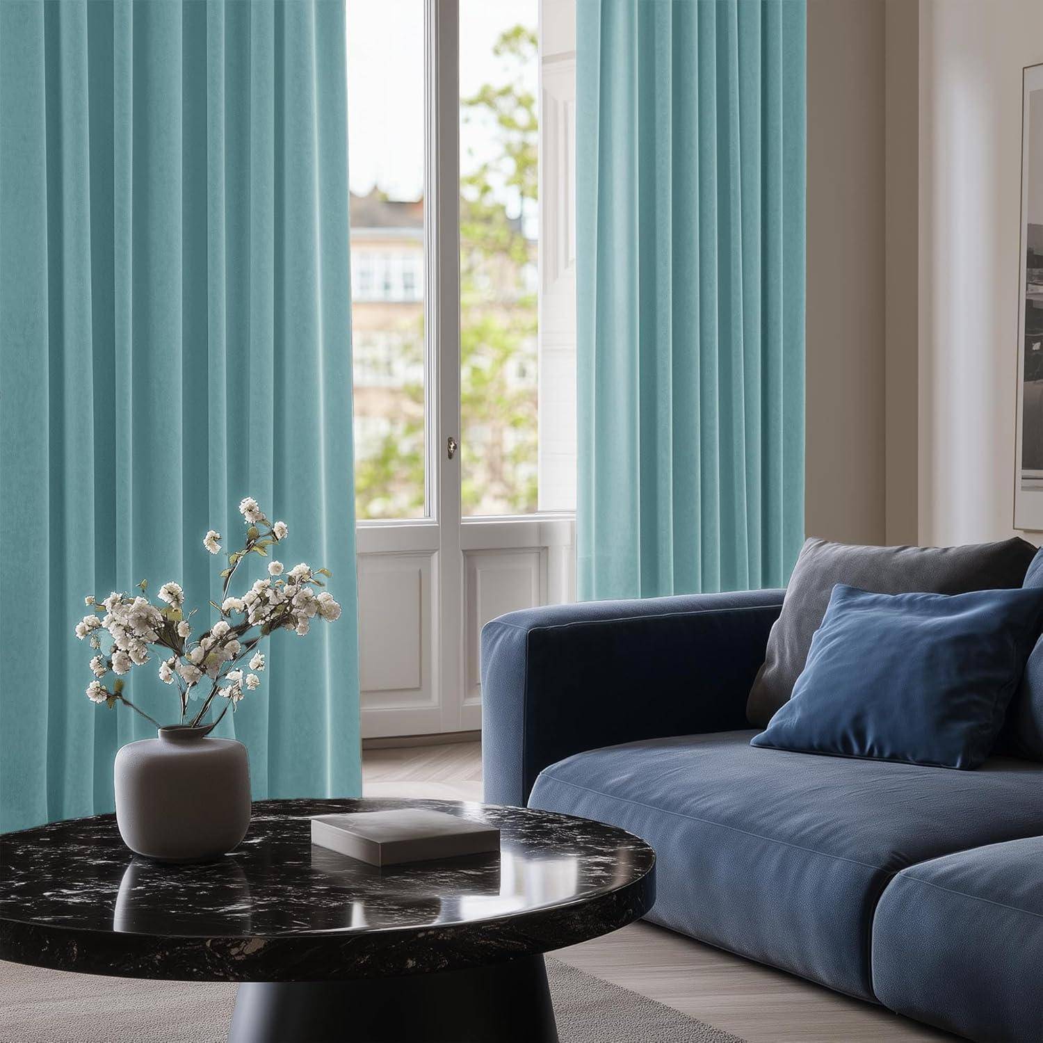 Ein gemütliches Wohnzimmer mit einem blauen Sofa, einem schwarzen Marmor-Couchtisch, auf dem eine Vase mit Blumen steht. Hellblaue Vorhänge verdecken die großen Fenster.