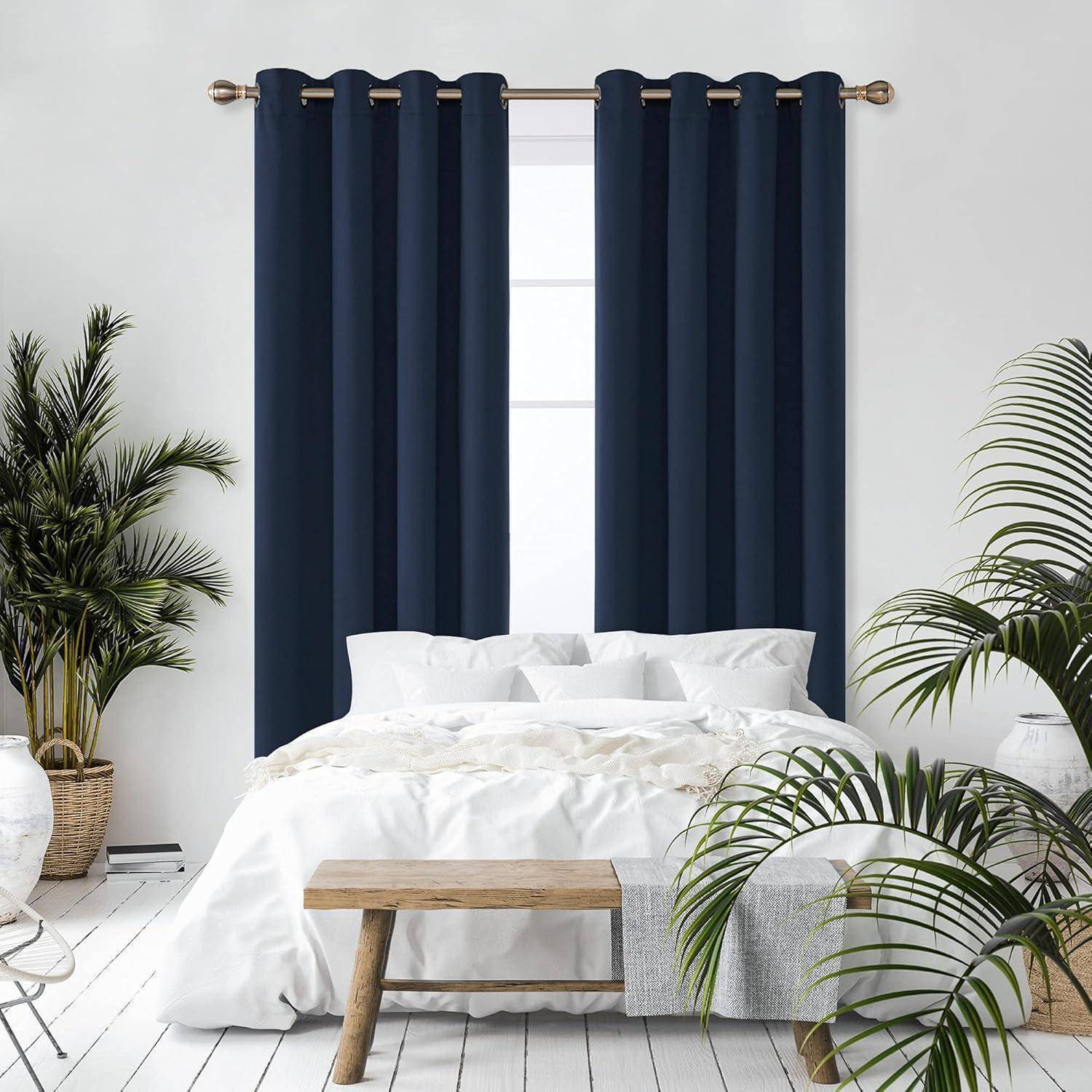 Ein ordentlich gemachtes Bett mit weißen Leinentüchern steht in einem hellen Raum. Dunkelblau Vorhänge bedecken das Fenster hinter dem Bett. Grüne Pflanzen säumen beide Seiten.