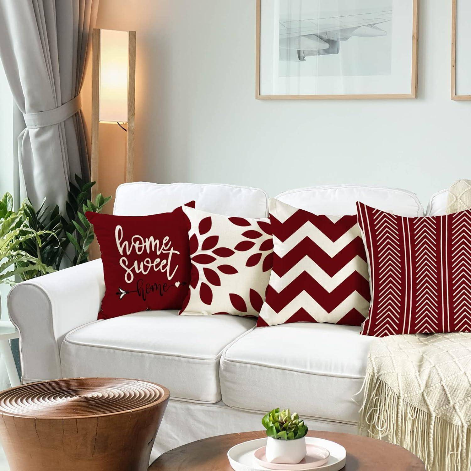 Ein gemütliches Wohnzimmer zeigt ein weißes Sofa mit roten und weißen Zierkissen, einen kleinen runden Couchtisch mit einer Pflanze und gerahmte Kunstwerke.