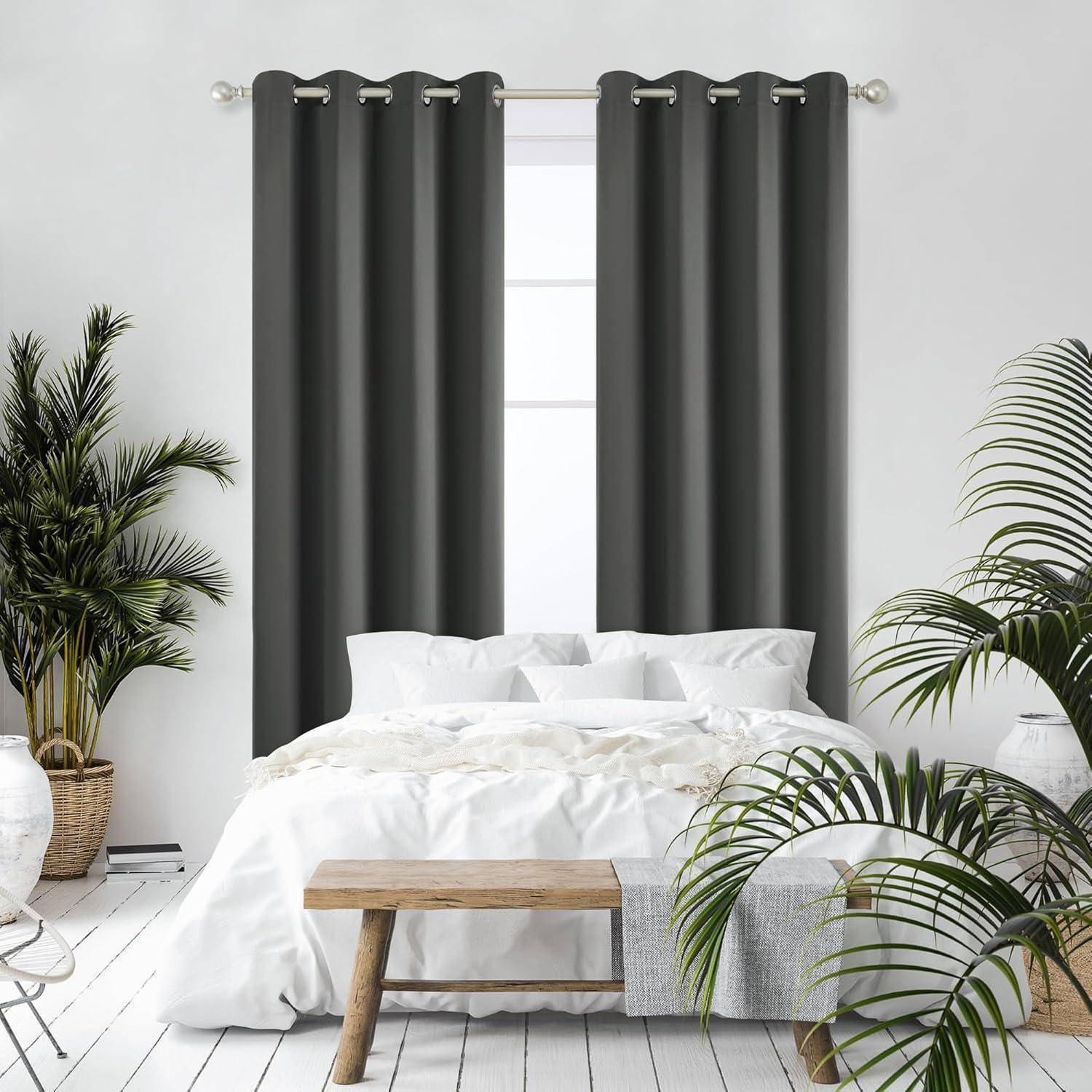 Gemütliches Schlafzimmer mit einem ordentlich gemachten weißen Bett, flankiert von Topfpflanzen auf einem Holzboden und dunklen Vorhängen, die ein großes Fenster umrahmen.