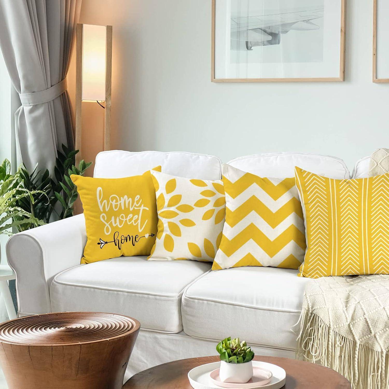 Ein gemütliches Wohnzimmer mit einem weißen Sofa, gelb-weißen gemusterten Kissen, einer kleinen Pflanze auf einem Holzcouchtisch und gerahmten Wandkunstwerken.