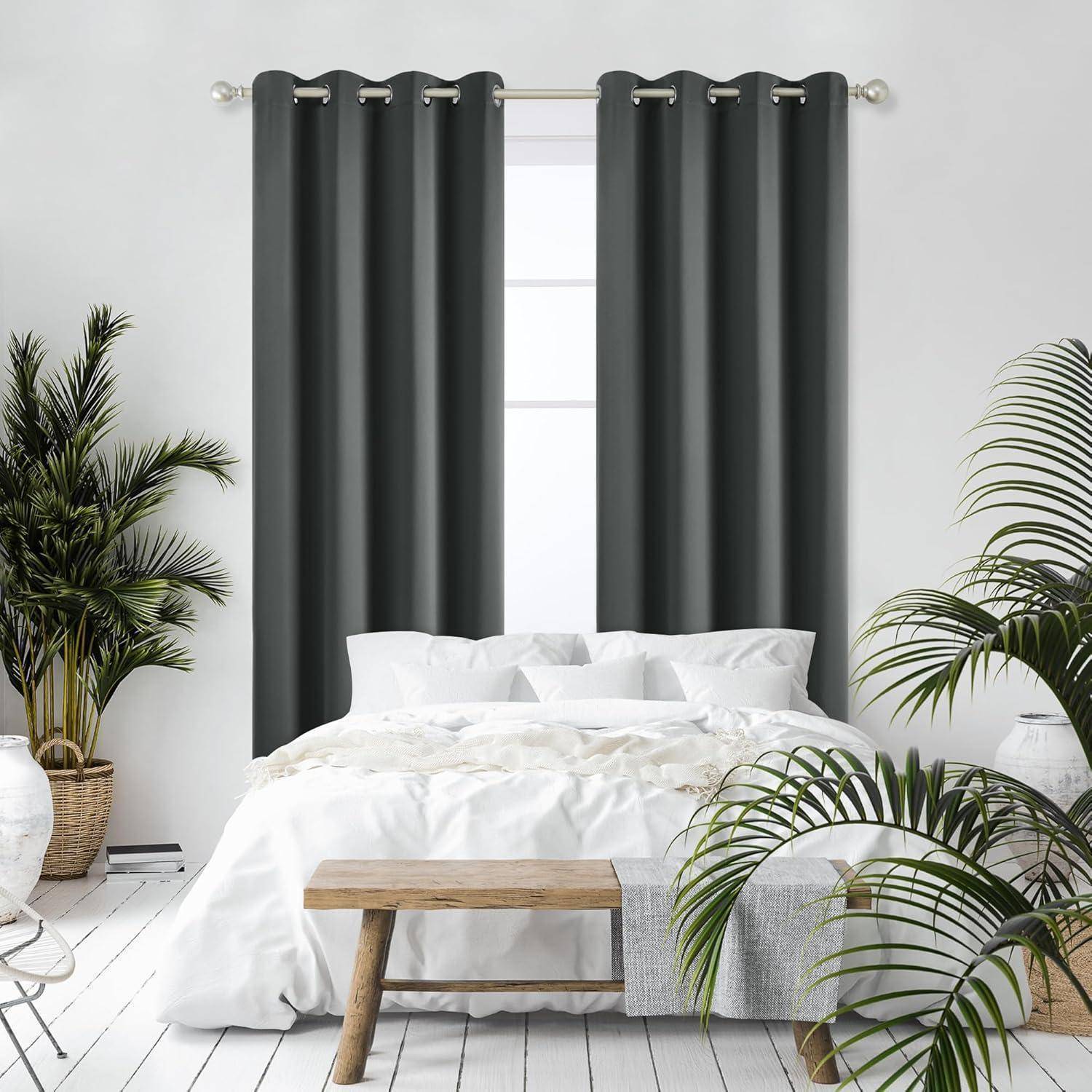 Ein gemütliches Schlafzimmer mit einem weißen Bett, einer Holzbank und Pflanzen, mit dunkelgrauen Vorhängen am Fenster, die eine friedliche Atmosphäre schaffen.