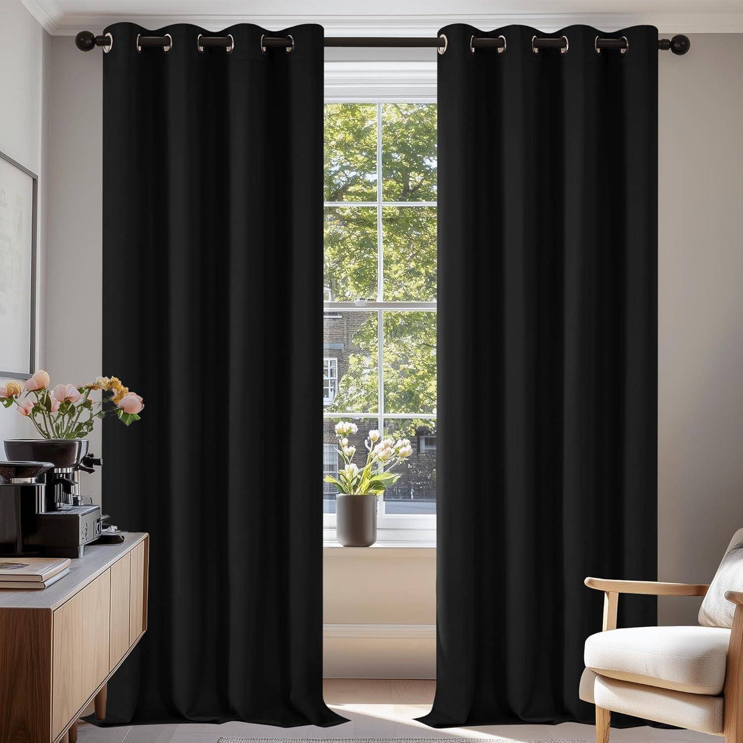 Ein Raum mit einem Fenster, das von schwarzen Vorhängen umrahmt ist, ein Holzschreibtisch mit Blumen und einer Kaffeemaschine auf der linken Seite und ein Stuhl auf der rechten Seite.