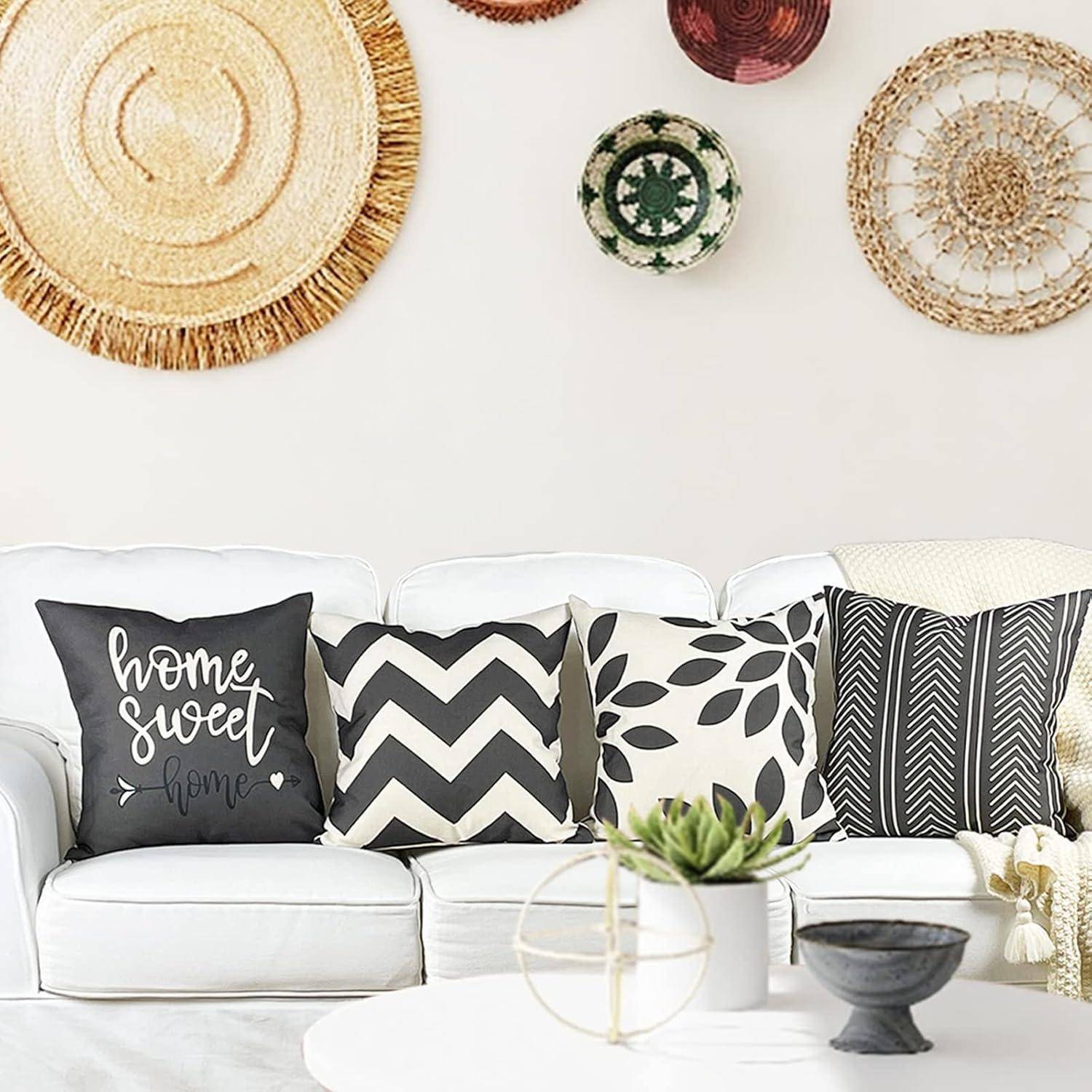 Ein gemütliches, modernes Wohnzimmer präsentiert ein weißes Sofa mit schwarz-weißen gemusterten Kissen. An den Wänden hängen gewebte Dekorationsgegenstände.