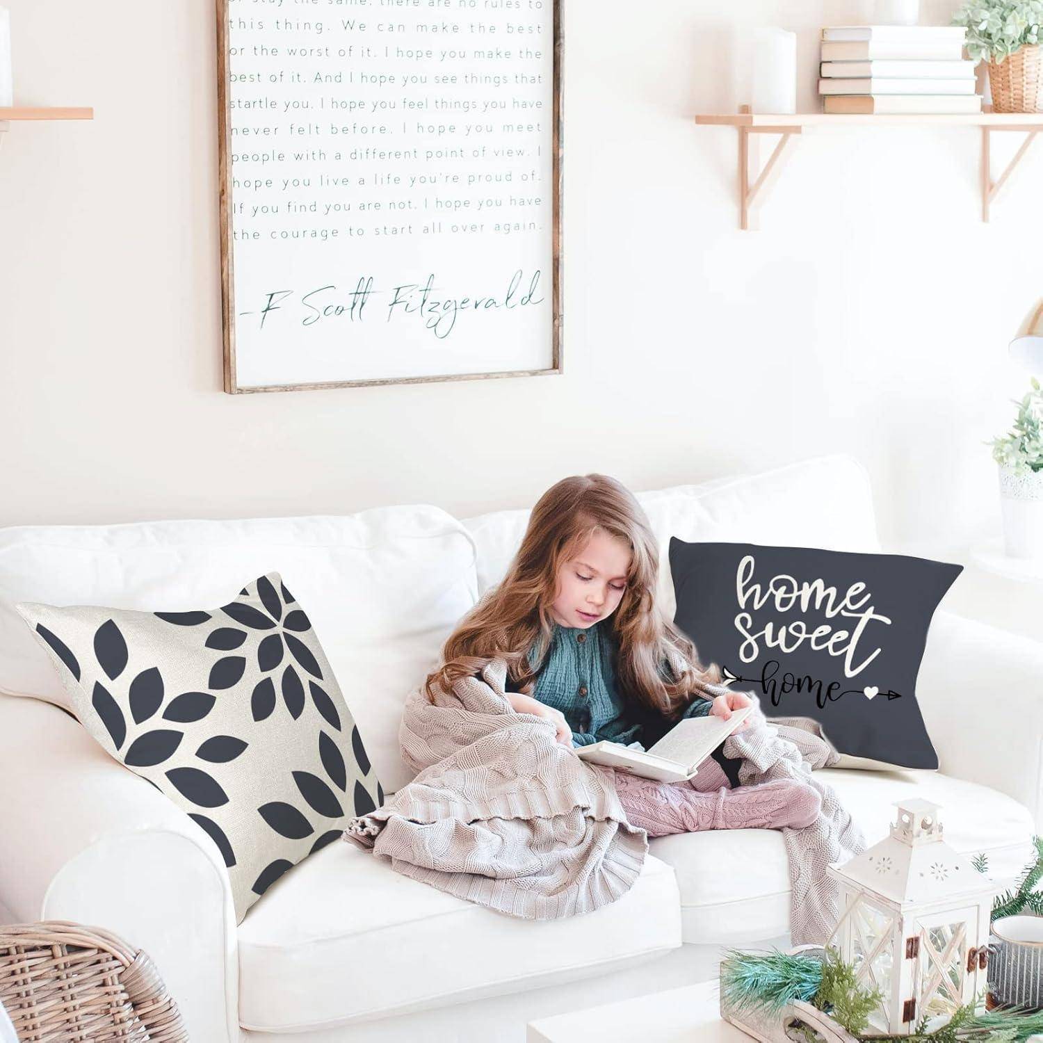 Ein junges Mädchen, in eine Decke gehüllt, sitzt auf einem weißen Sofa und liest ein Buch. Ein Kissen neben ihr trägt die Aufschrift „Home sweet home
