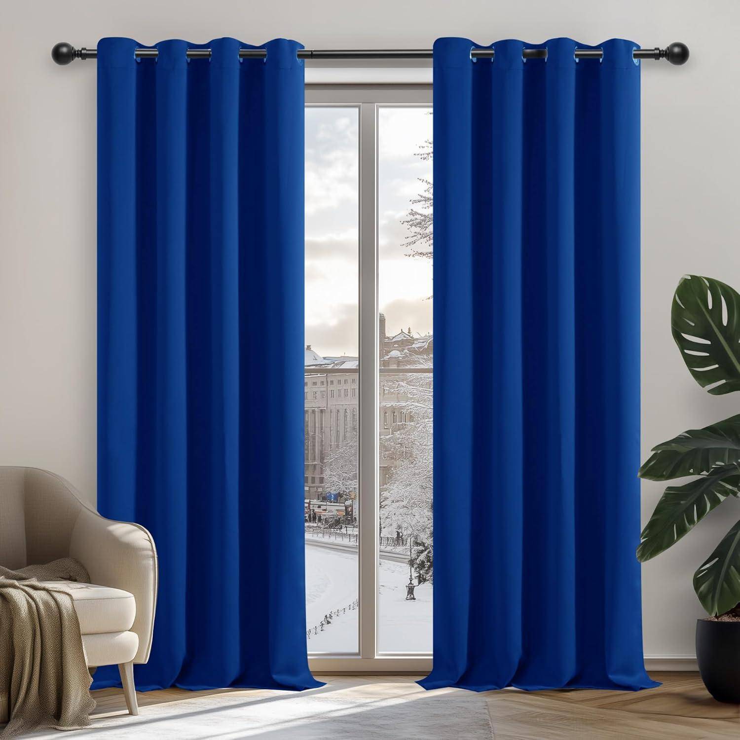 Ein Wohnzimmer mit blauen Vorhängen, die ein Fenster umrahmen, durch das eine verschneite Straße zu sehen ist. Auf der linken Seite steht ein beiger Sessel mit einer Decke, rechts eine Pflanze.
