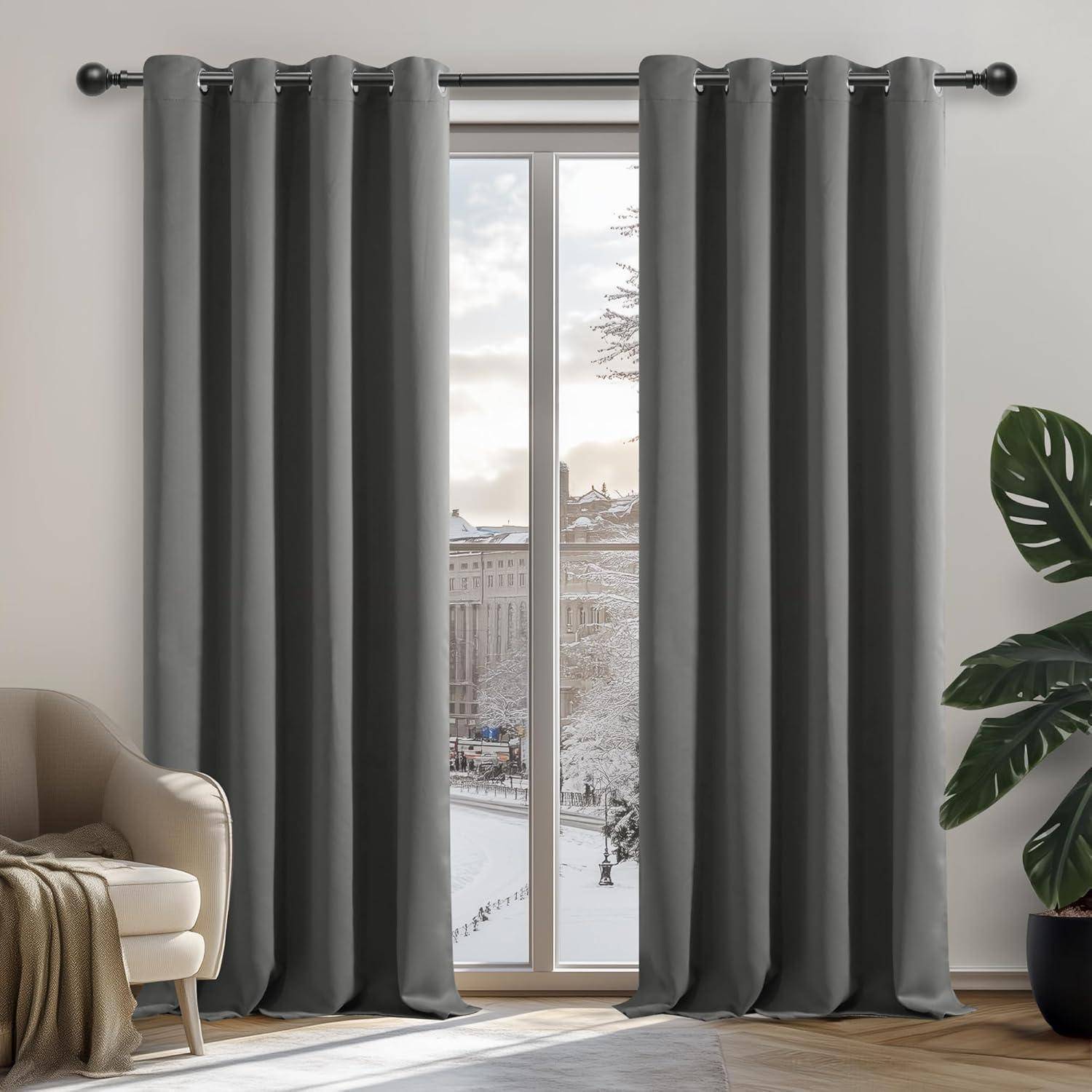 Ein Wohnzimmerfenster mit grauen Vorhängen blickt auf eine verschneite Straße, die von Gebäuden und Bäumen umrahmt wird. Ein beiger Sessel und eine Pflanze befinden sich in der Nähe.